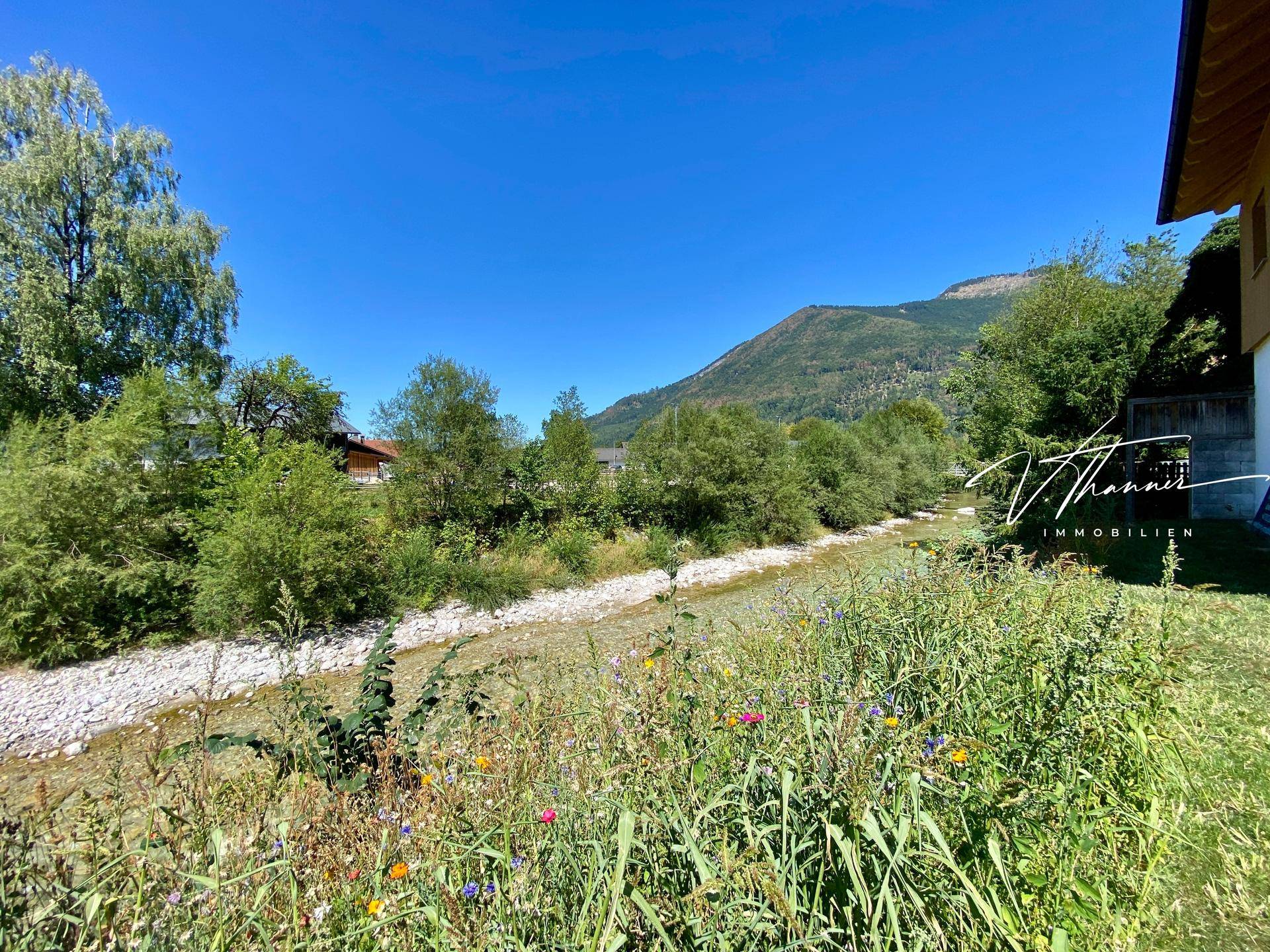 Malerischer Blick auf den Fluss und die umliegende grüne Landschaft mit Bergen im Hintergrund.