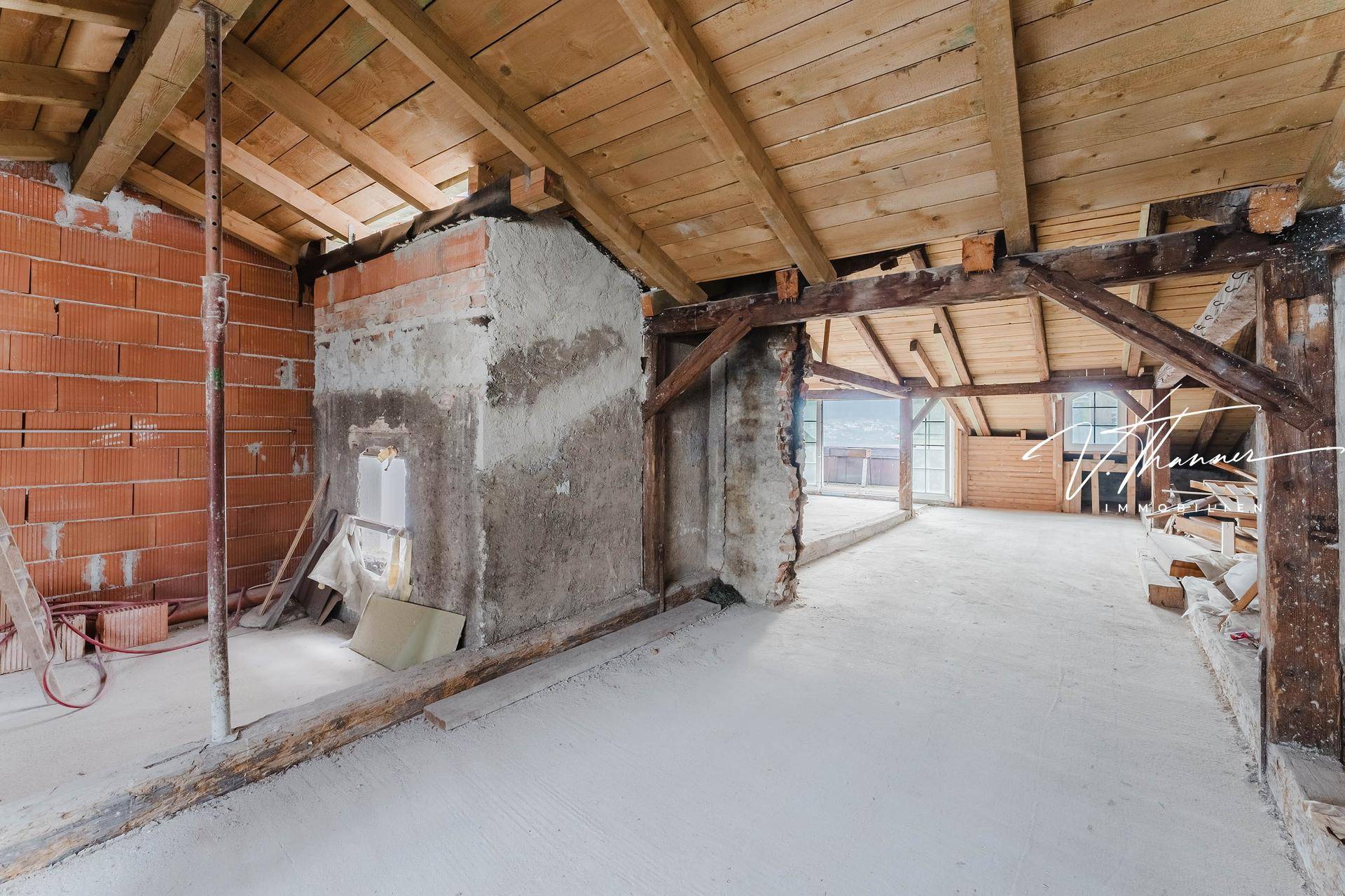 Unfertiger Dachbodenraum mit sichtbaren Holzbalken, Ziegelwänden und viel Potenzial für den Ausbau.