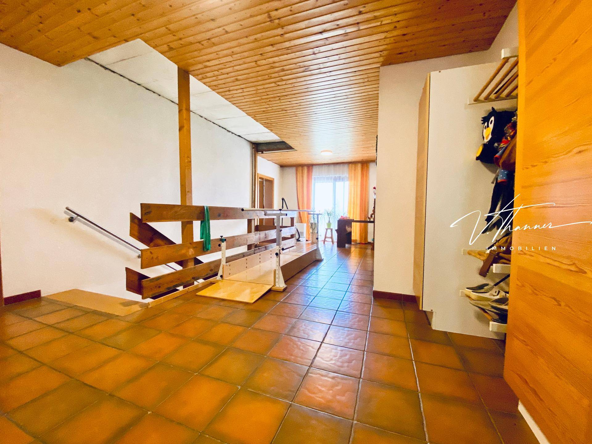 Geräumiger Flur mit Fliesenboden, Holzdecke und einem Treppenlift für Barrierefreiheit.