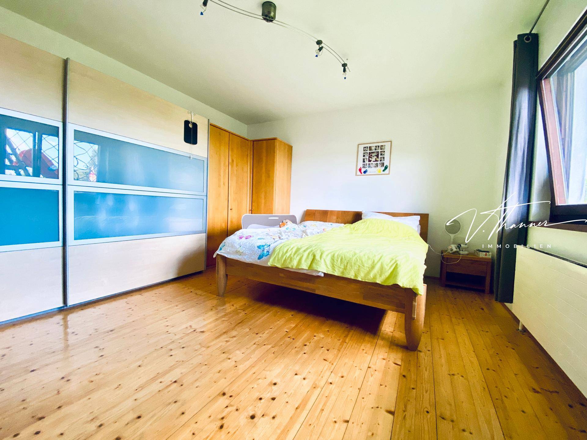Helles Schlafzimmer mit Holzboden, großem Kleiderschrank und Fenster mit Ausblick.