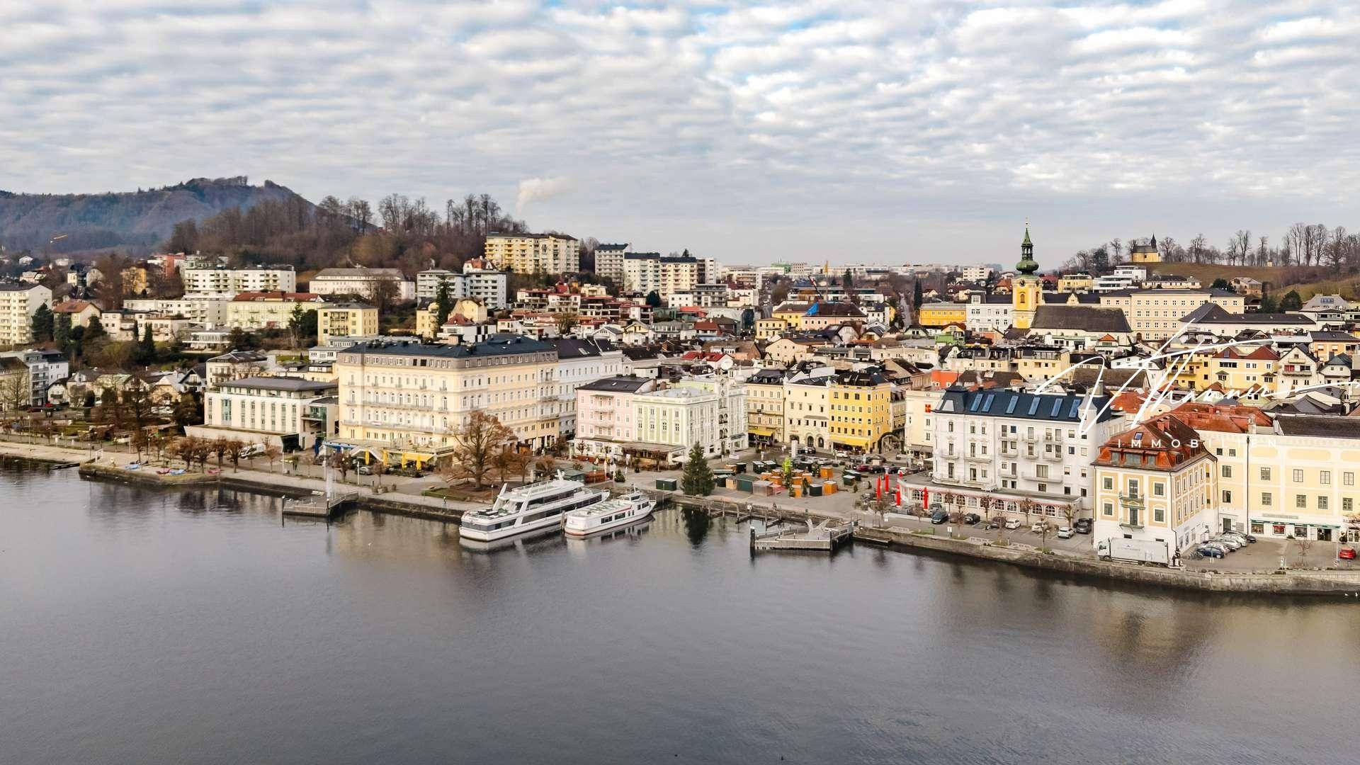 Weitläufige Ansicht der Stadt am Seeufer mit zahlreichen Gebäuden und Schiffsanlegestellen.