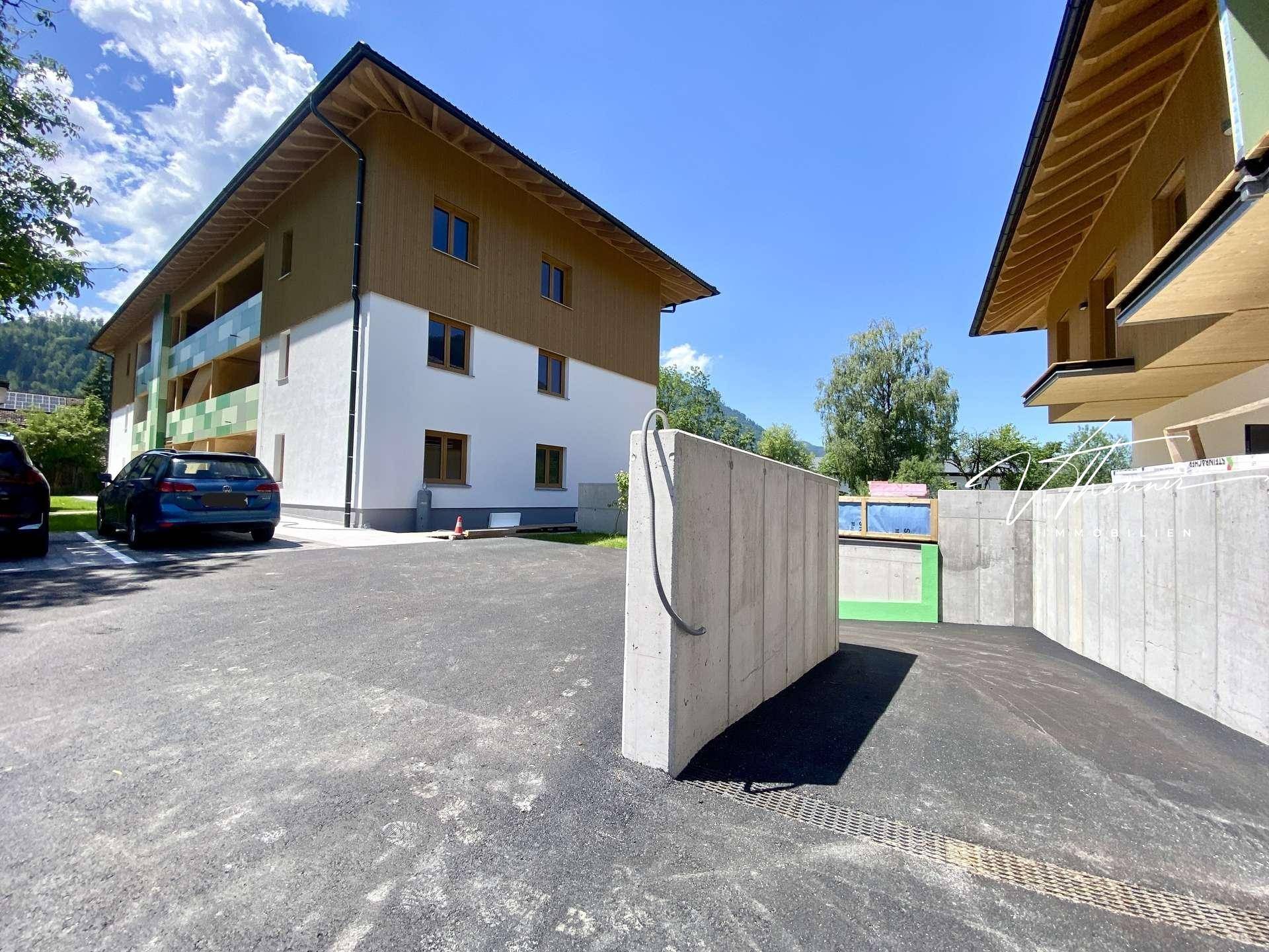 Außenansicht der Wohnanlage mit Parkplätzen und Zufahrt, umgeben von grüner Landschaft.