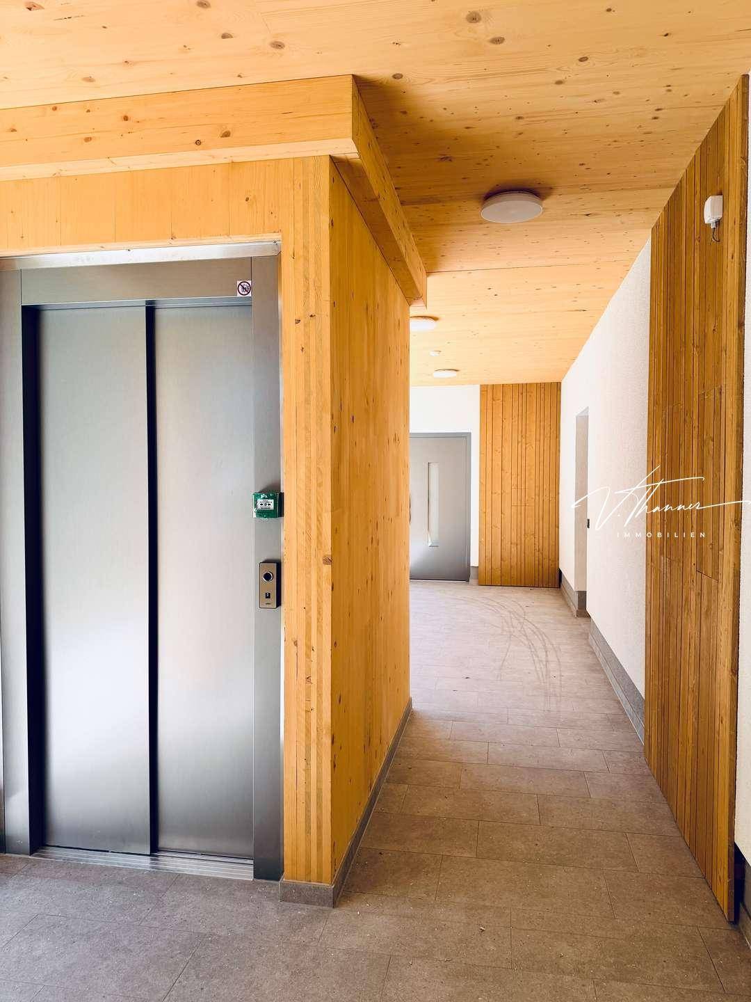 Moderner Flur mit Holzverkleidung und einem Aufzug in einem neu errichteten Gebäude.
