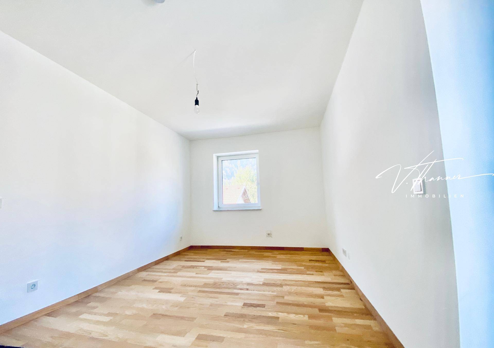 Helles Schlafzimmer mit Holzboden und einem Fenster, bereit zur individuellen Gestaltung.