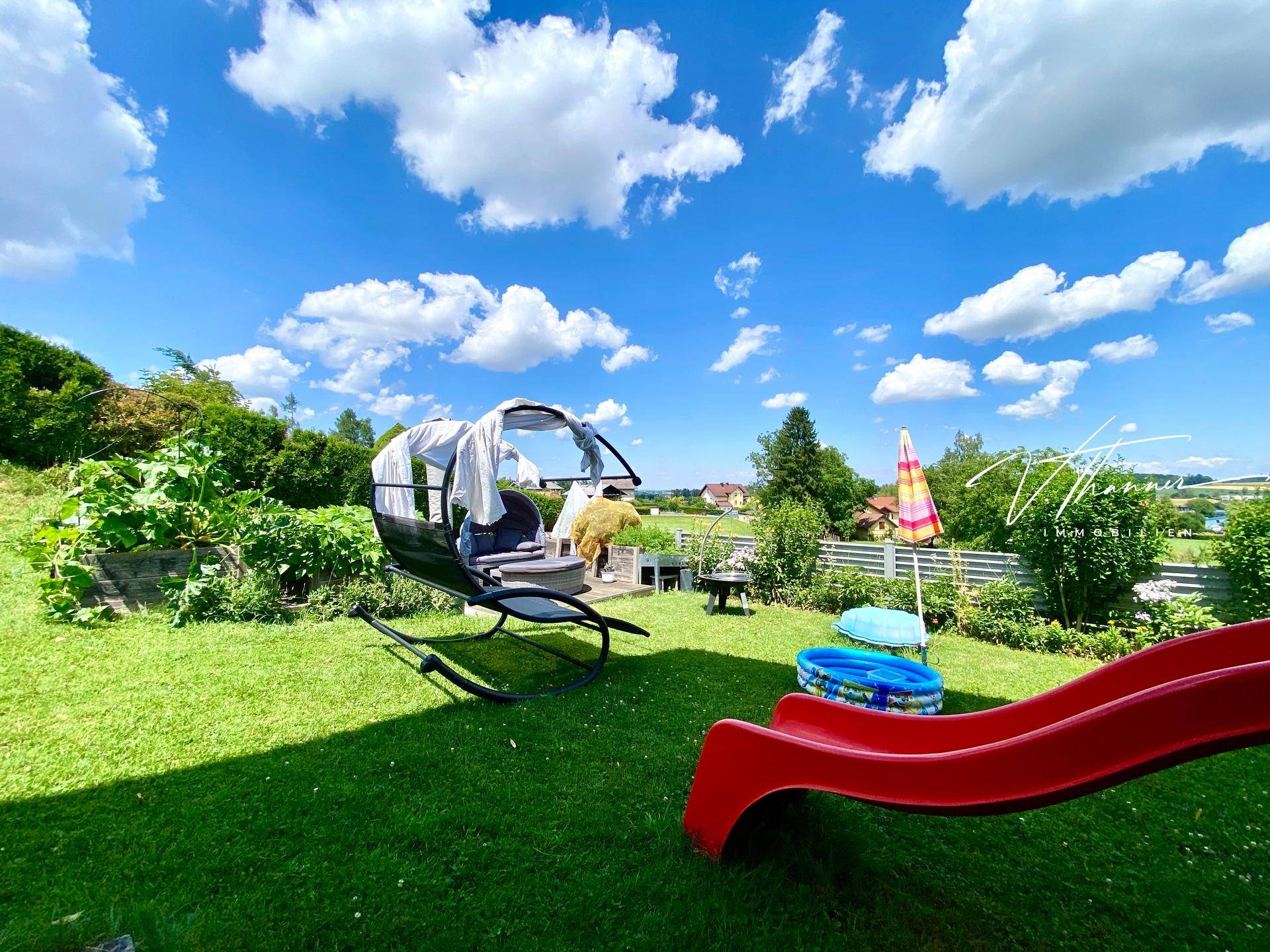 Sonniger Gartenbereich mit Rasenfläche, Kinderrutsche und einem Outdoor-Sitzmöbel.