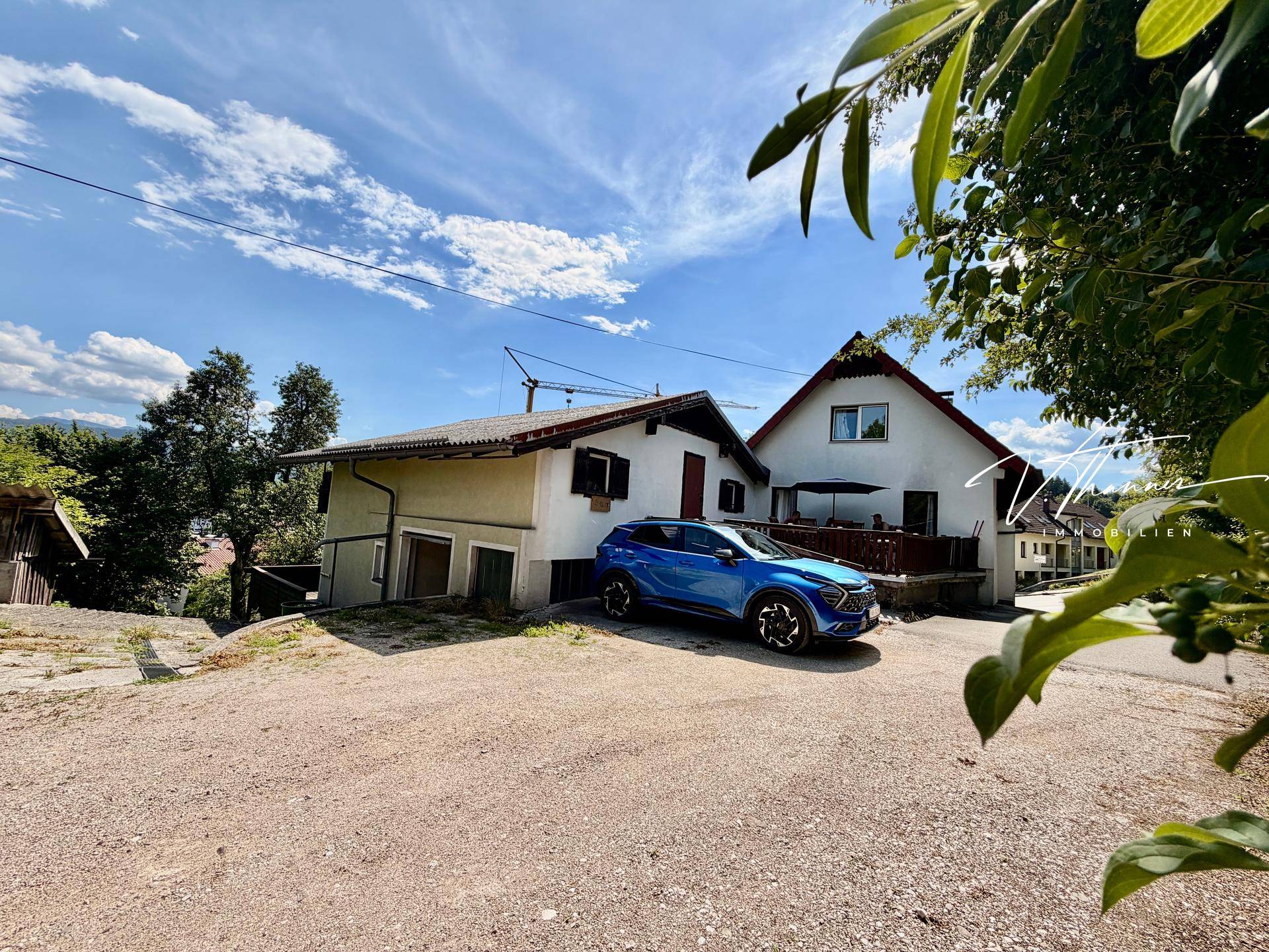 Seitenansicht des Hauses mit geparktem Auto auf der Kiesauffahrt und umgebender Natur.