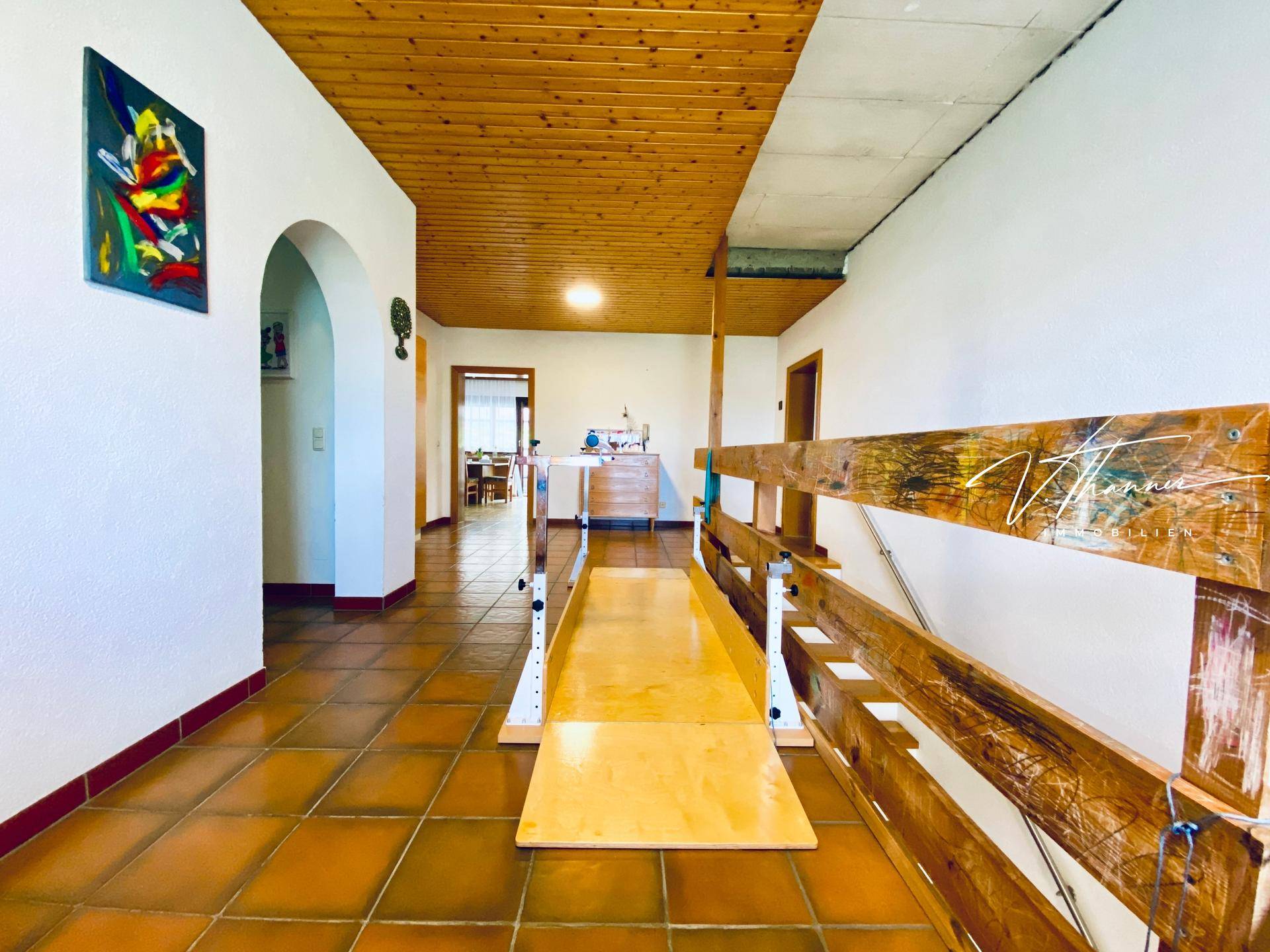 Heller Flur im Obergeschoss mit Fliesenboden, Holzdecke und einem Treppenlift.