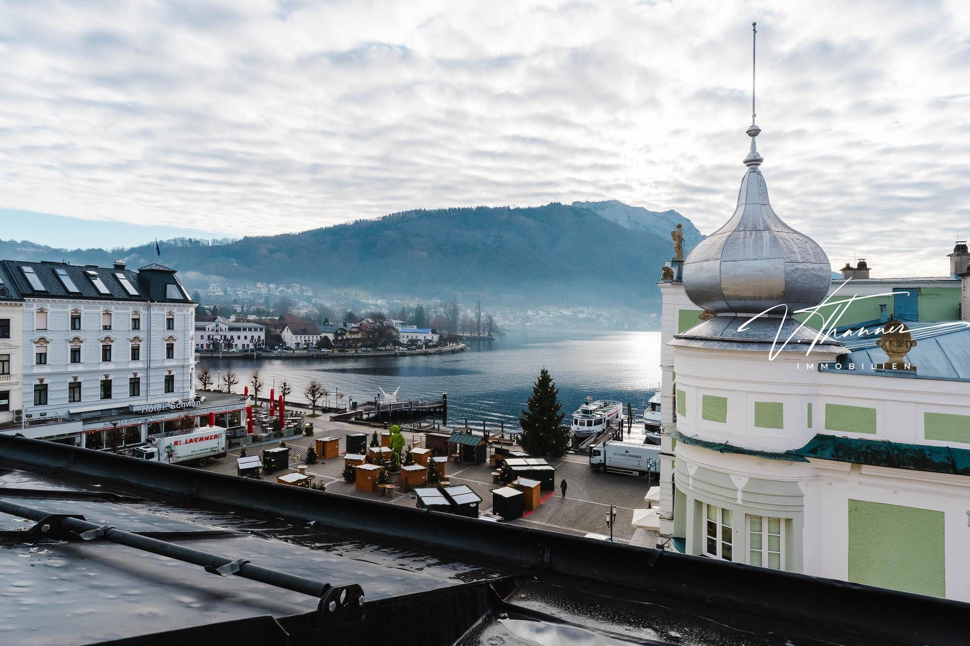 Panoramablick von einem Dach über die Stadt und den See mit Bergen im Hintergrund.