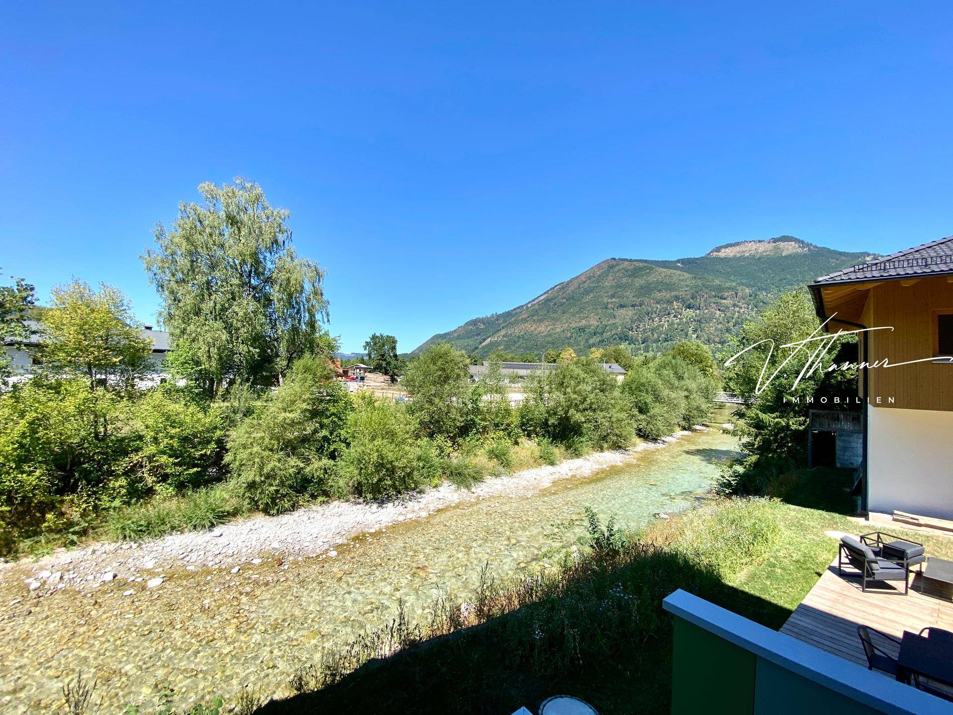 Panoramablick von einem Balkon auf den klaren Fluss und die umliegenden Berge unter blauem Himmel.