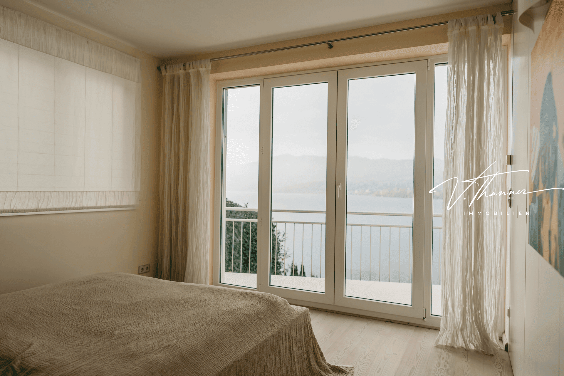 Schlafzimmer mit Bett und großen Fenstern, die einen weiten Blick auf den See bieten.
