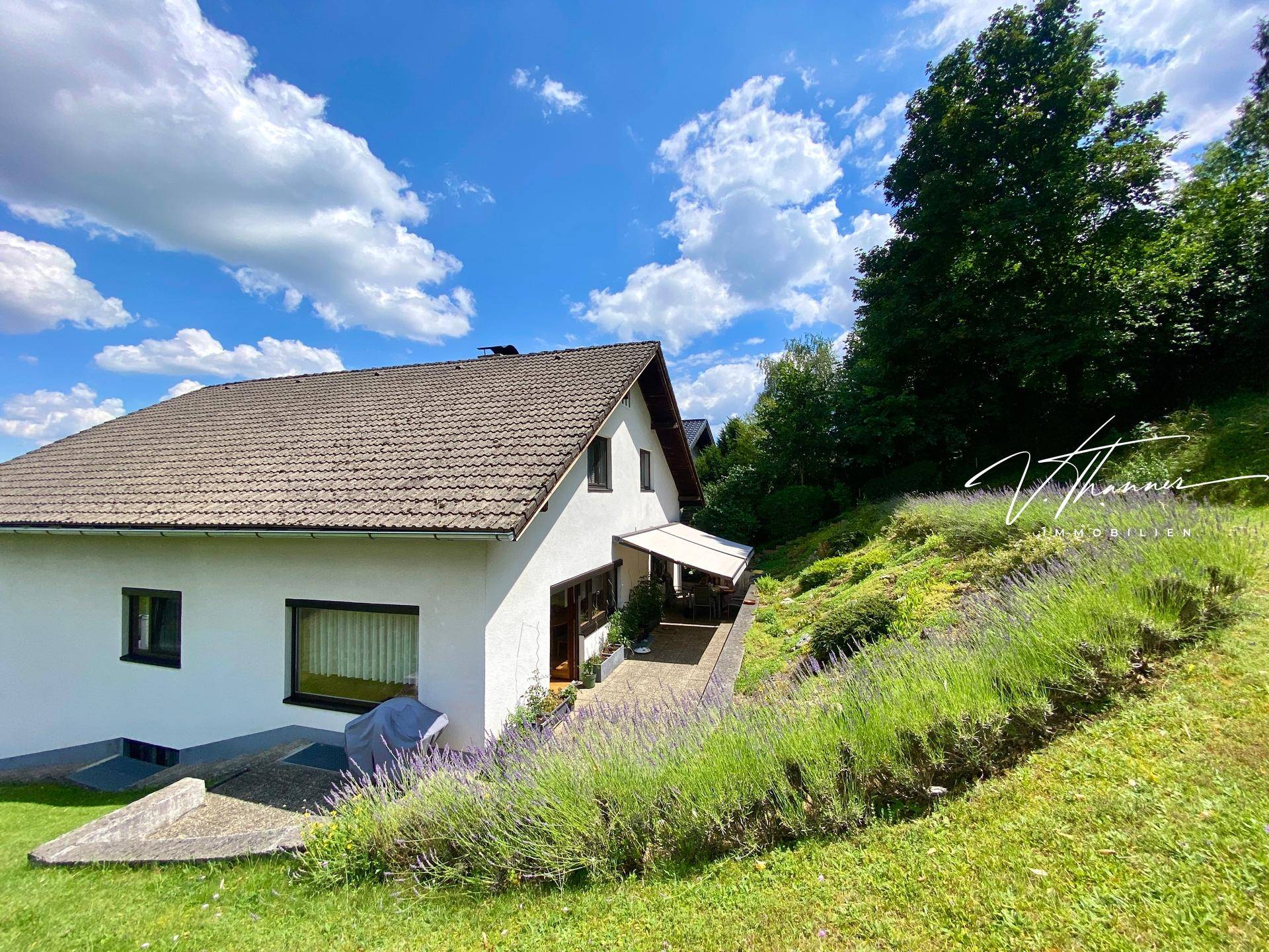 Seitenansicht des Hauses mit überdachter Terrasse und einem gepflegten Gartenbereich am Hang.