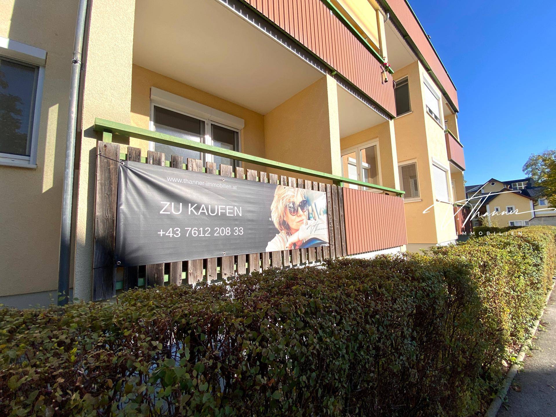 Balkon mit Werbebanner "ZU KAUFEN" und Blick auf die grüne Umgebung des Wohnhauses.