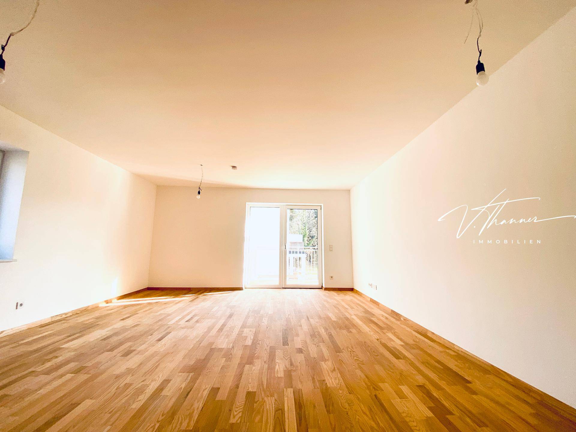 Heller, leerer Raum mit Holzboden und Zugang zu einem Balkon oder einer Terrasse.
