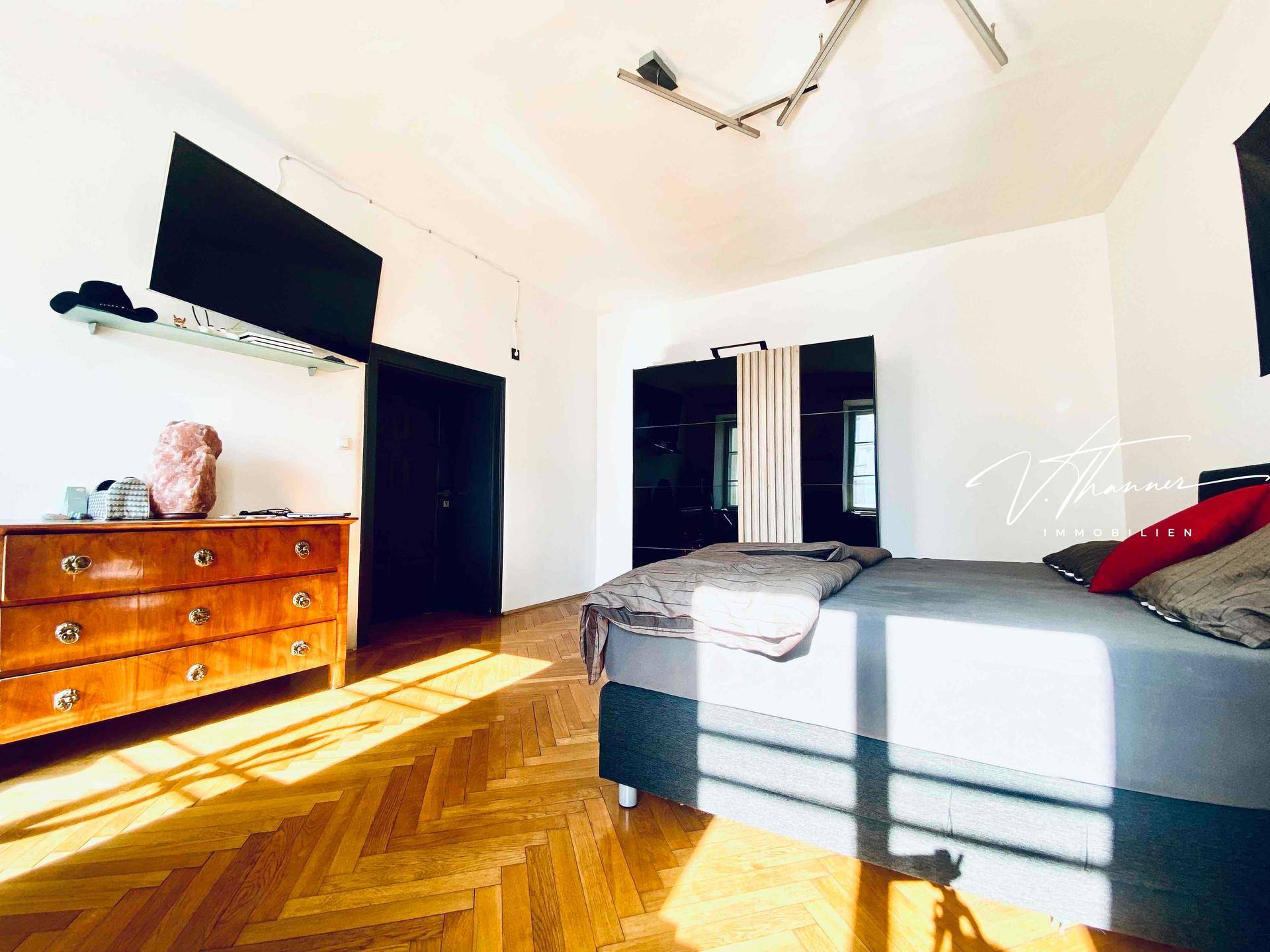 Helles Schlafzimmer mit Fischgrätparkettboden, modernem Kleiderschrank und viel natürlichem Licht.