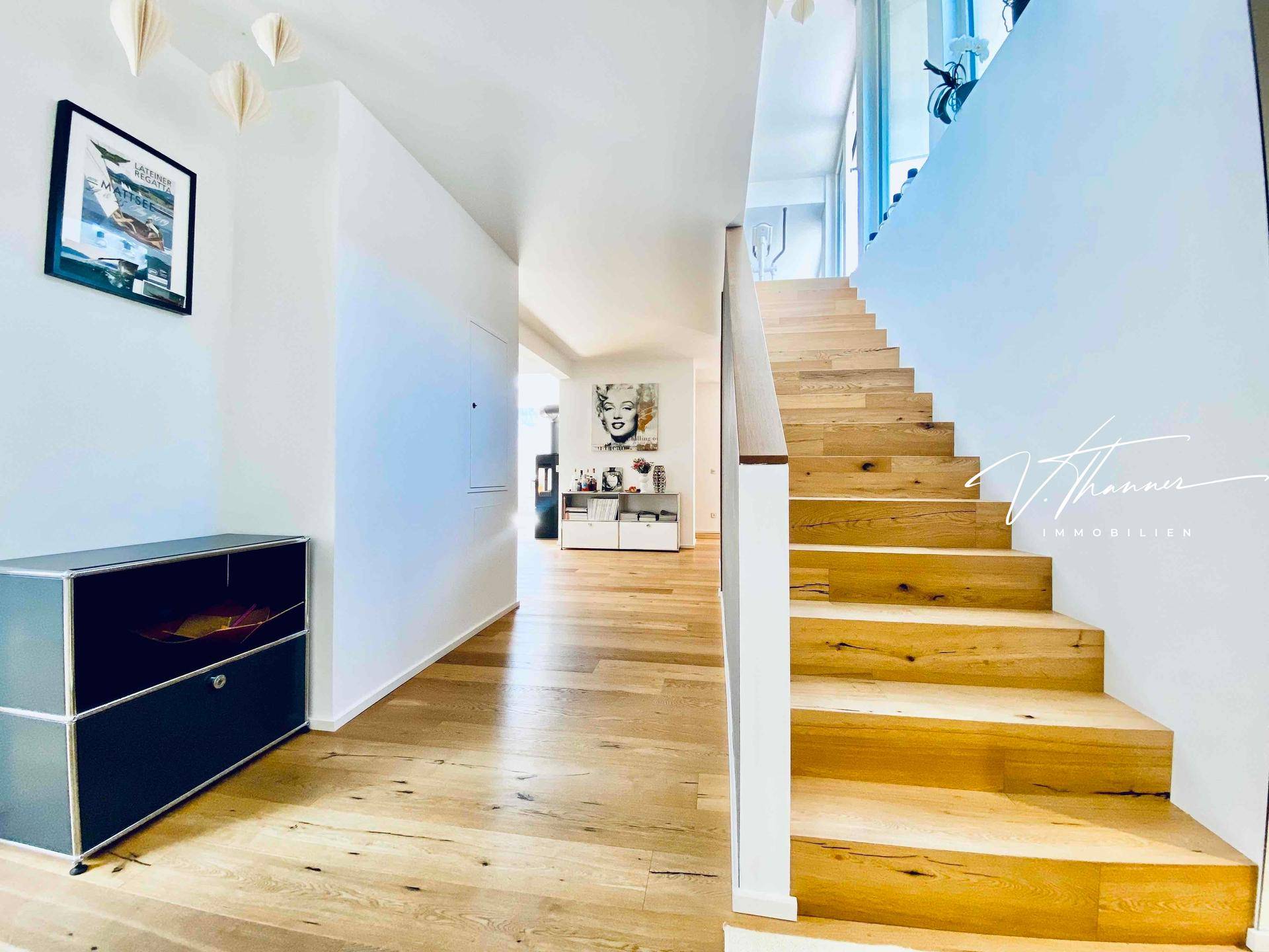 Heller Eingangsbereich mit Holztreppe und modernem Design, der zu den oberen Etagen führt.