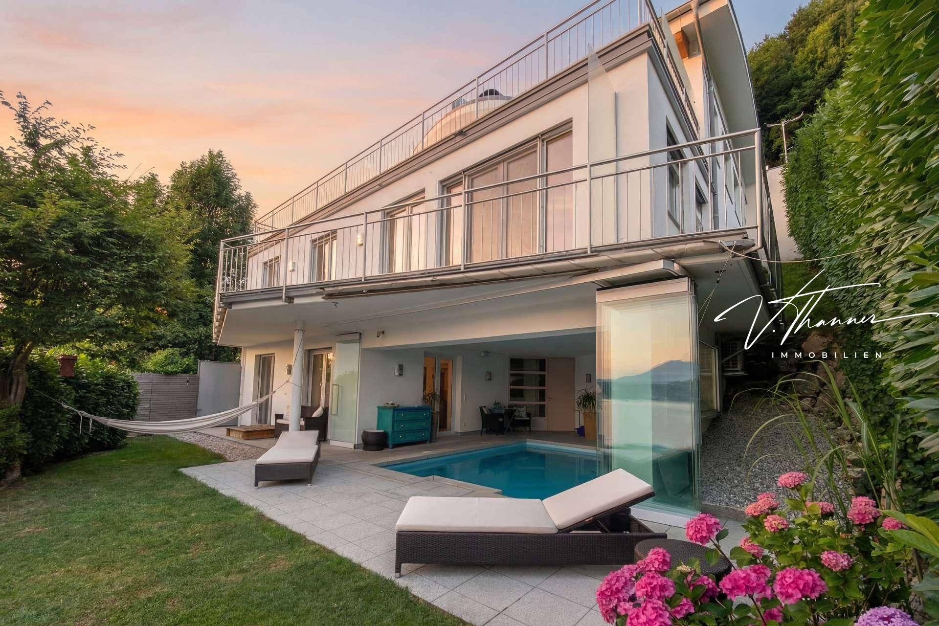 Moderne Villa mit Garten, Poolbereich und mehreren Balkonen, eingebettet in eine grüne Landschaft mit Seeblick.