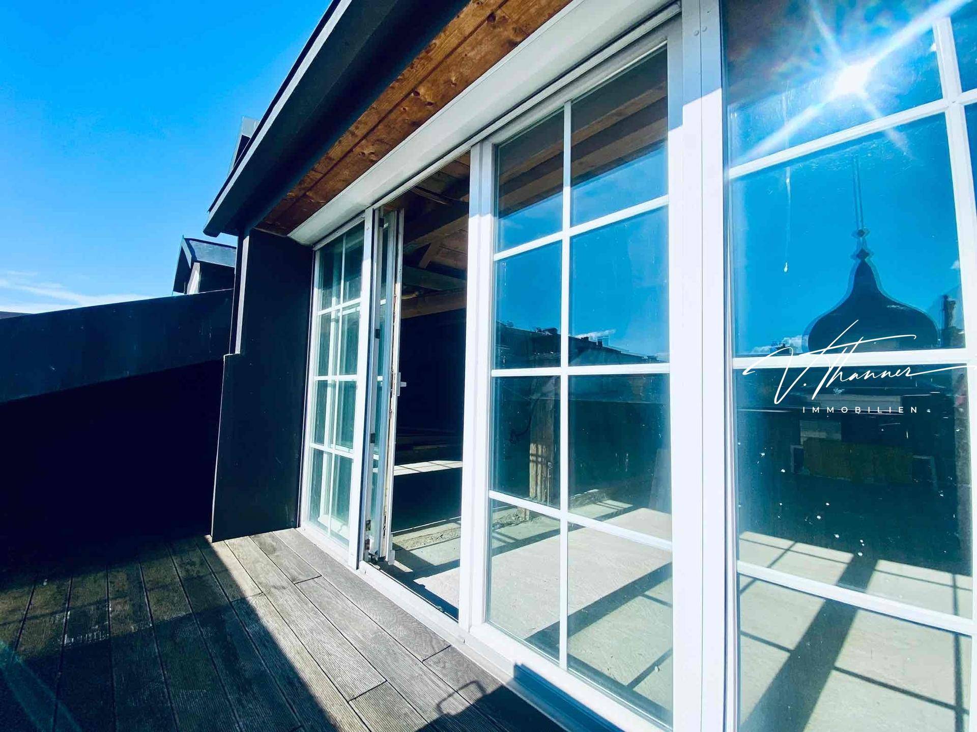 Sonnige Terrasse mit Holzboden und großen Fenstern, die viel Licht in den Innenraum lassen.