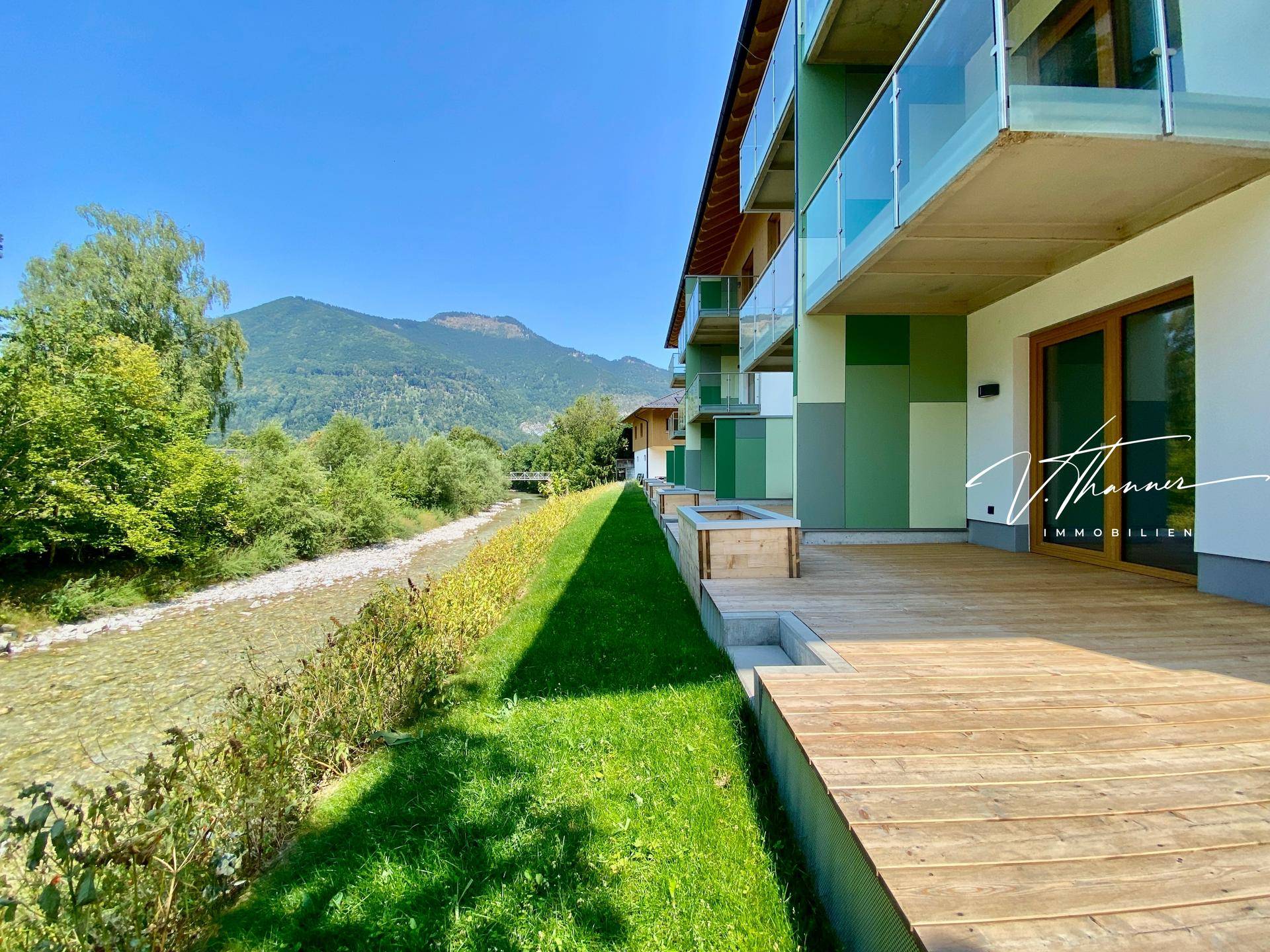 Reihen von Terrassen mit Holzboden entlang des Gebäudes, direkt am Flussufer mit Bergblick.