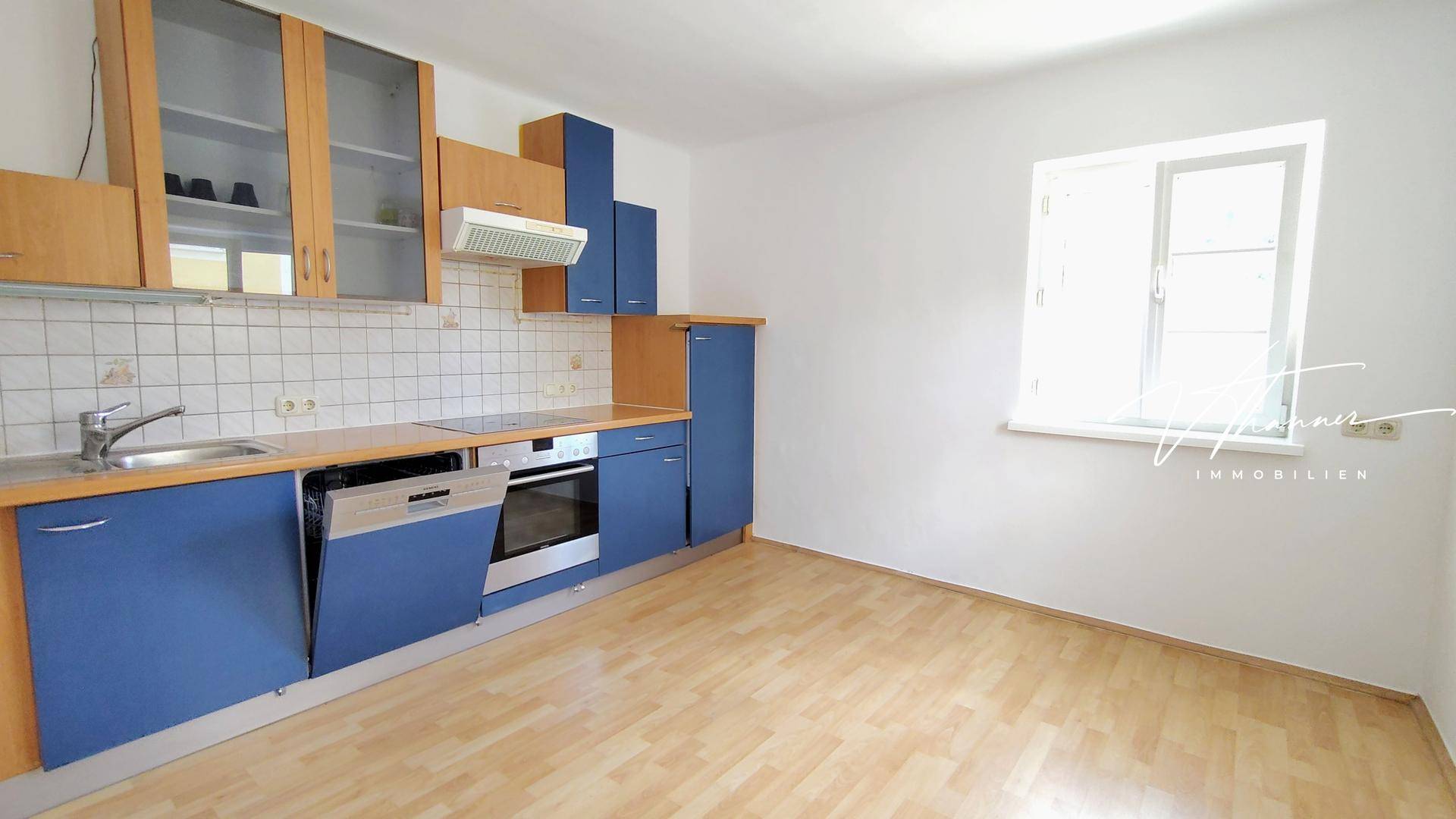 Einbauküche mit blauen und holzfarbenen Schränken, integrierten Geräten und Fenster.