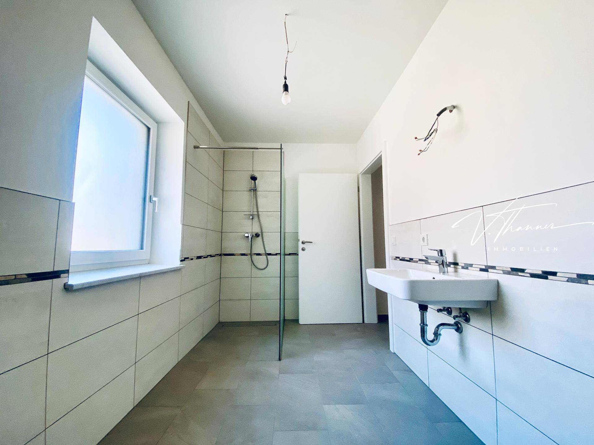 Modernes Badezimmer mit Dusche, Waschbecken und Fenster, noch in Fertigstellung.