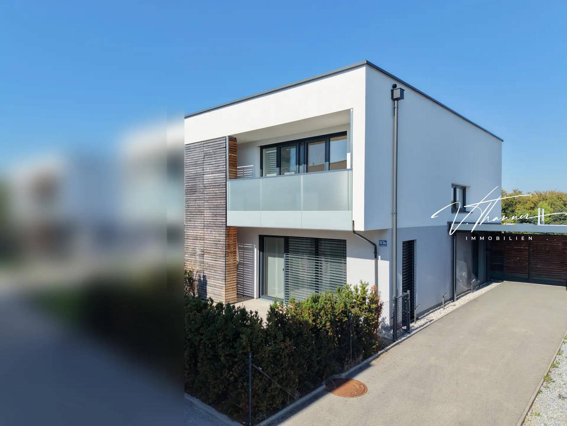Moderne Hausfassade mit Holzelementen, Balkon mit Glasbrüstung und gepflegter Auffahrt.