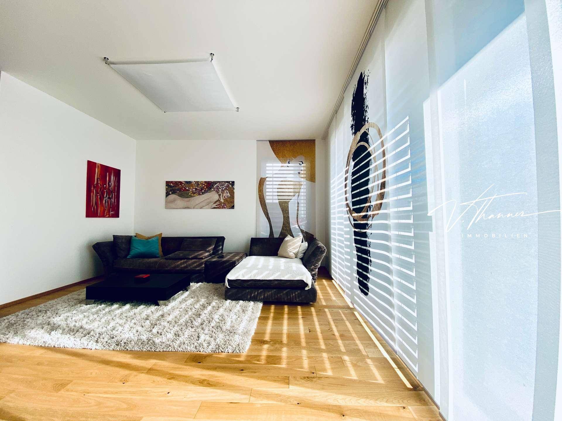 Lichtdurchflutetes Wohnzimmer mit Parkettboden, modernen Vorhängen und Kunstwerken an der Wand.