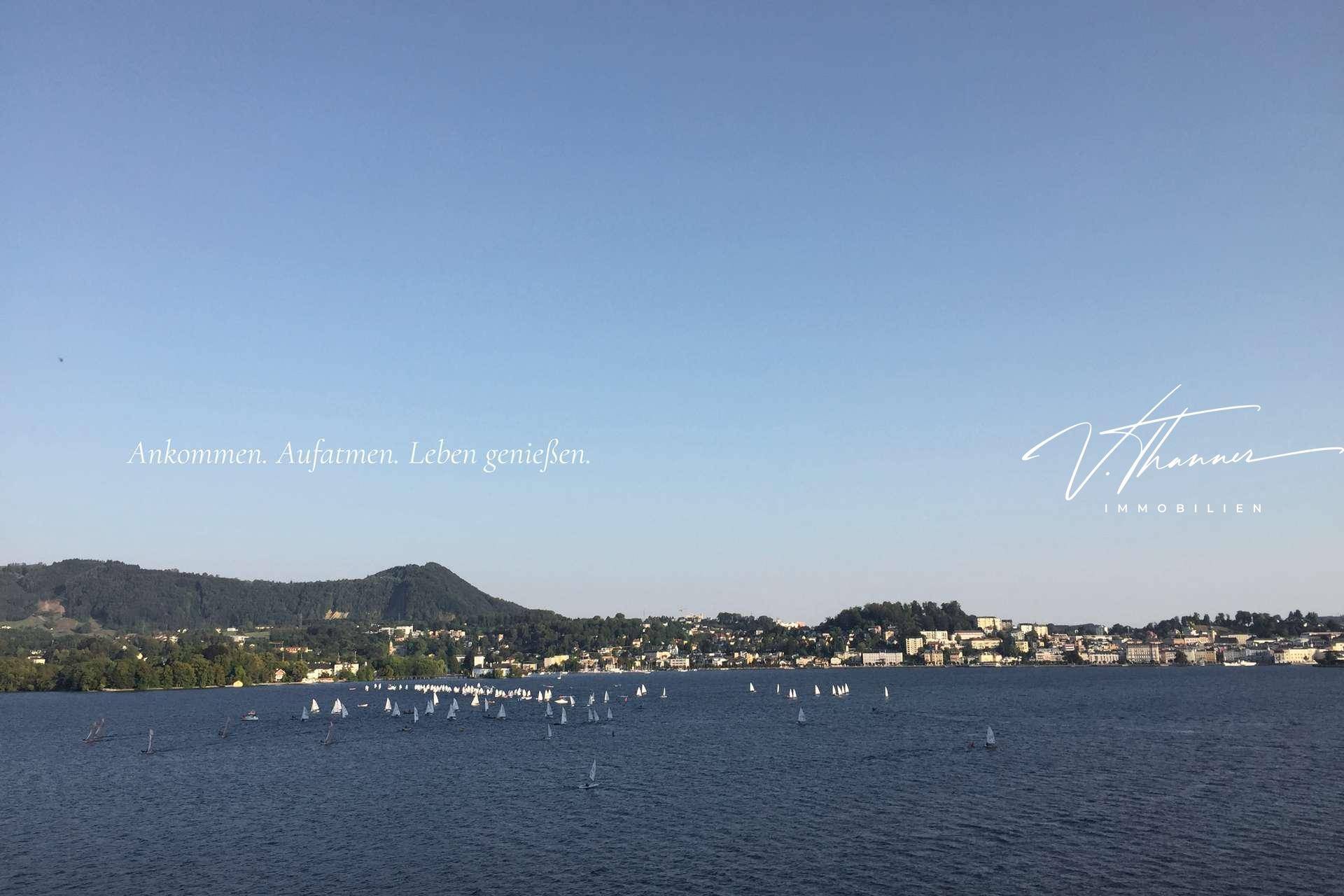 Weitläufiger Seeblick mit zahlreichen Segelbooten und majestätischen Bergen im Hintergrund.