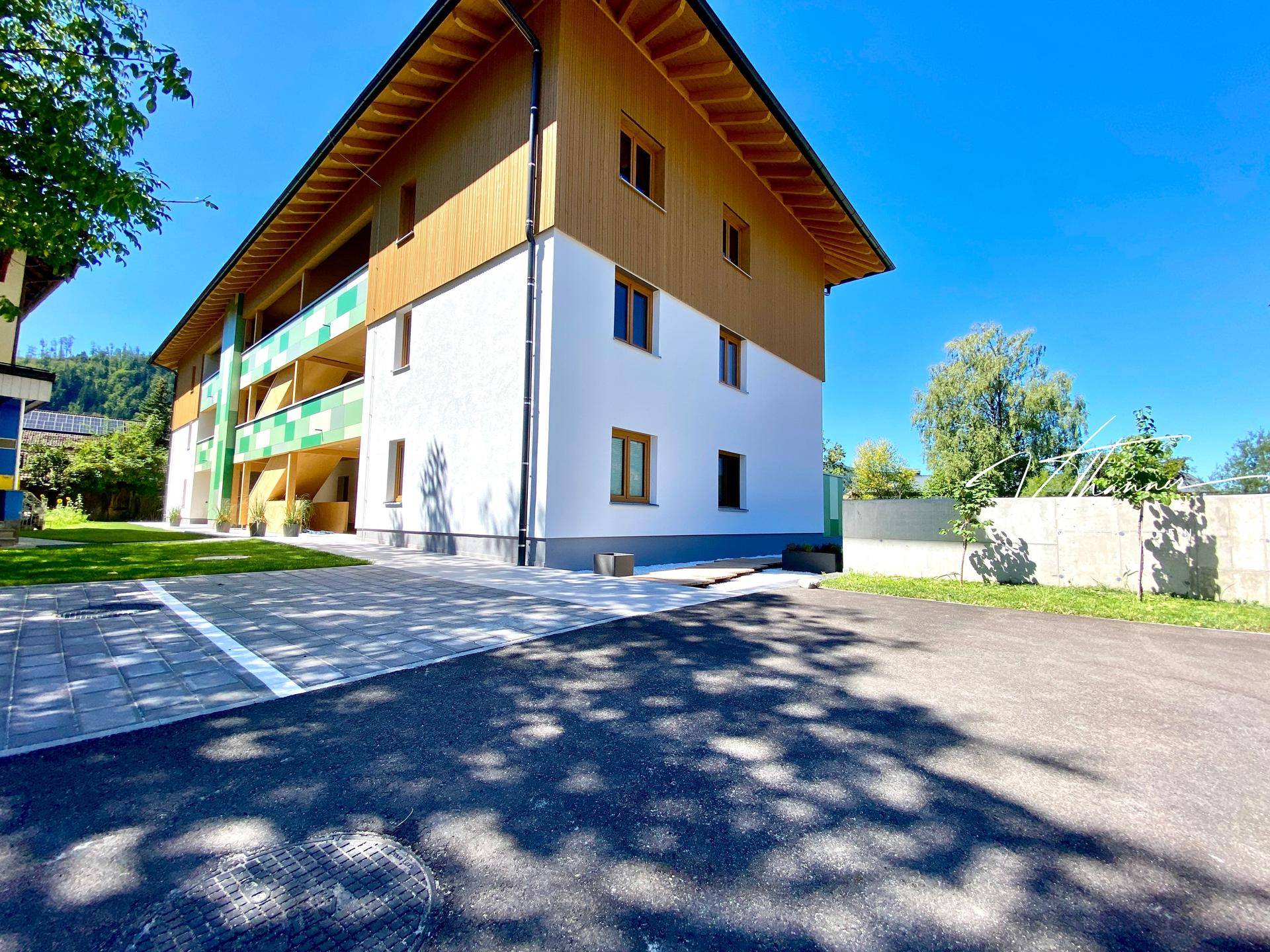 Außenansicht der Wohnanlage mit Parkplatz und moderner Architektur unter blauem Himmel.