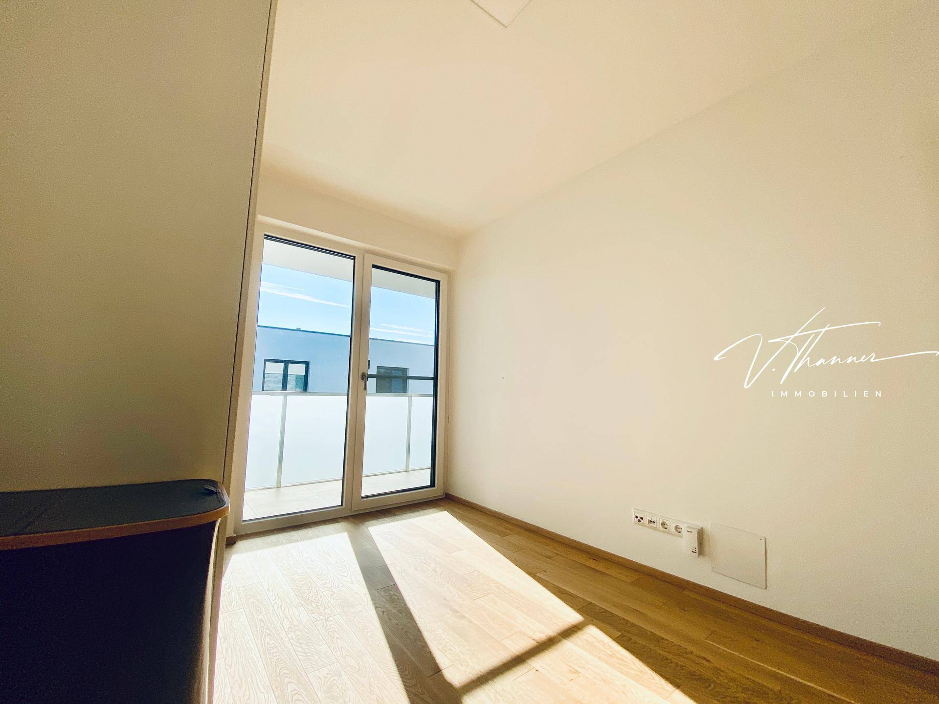 Helles Zimmer mit Parkettboden und Zugang zu einem Balkon oder einer Terrasse.