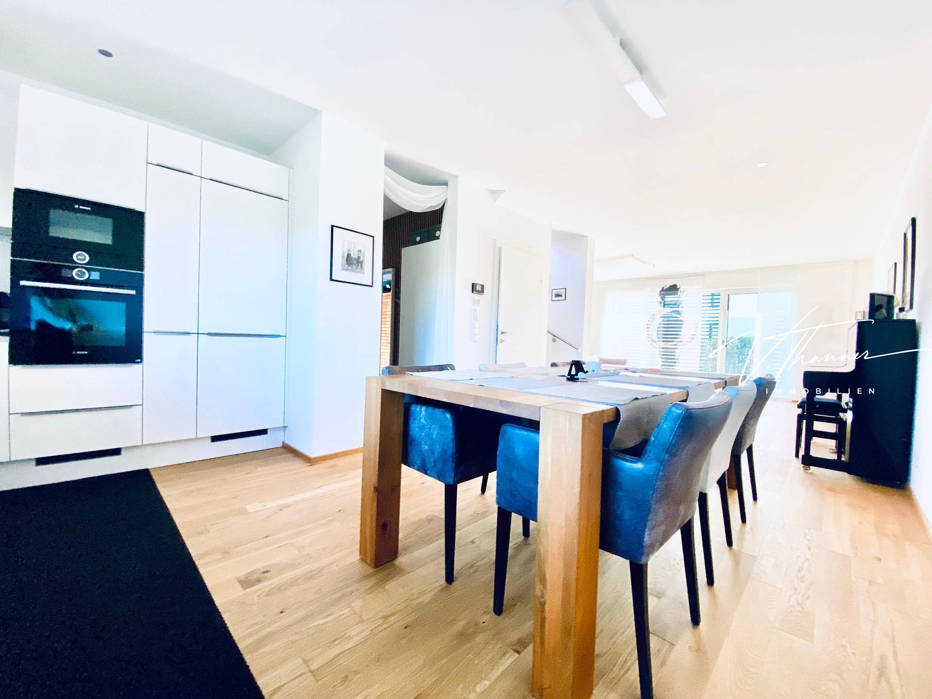 Moderne Einbauküche mit weißen Schränken, Holztisch und integrierten Geräten.
