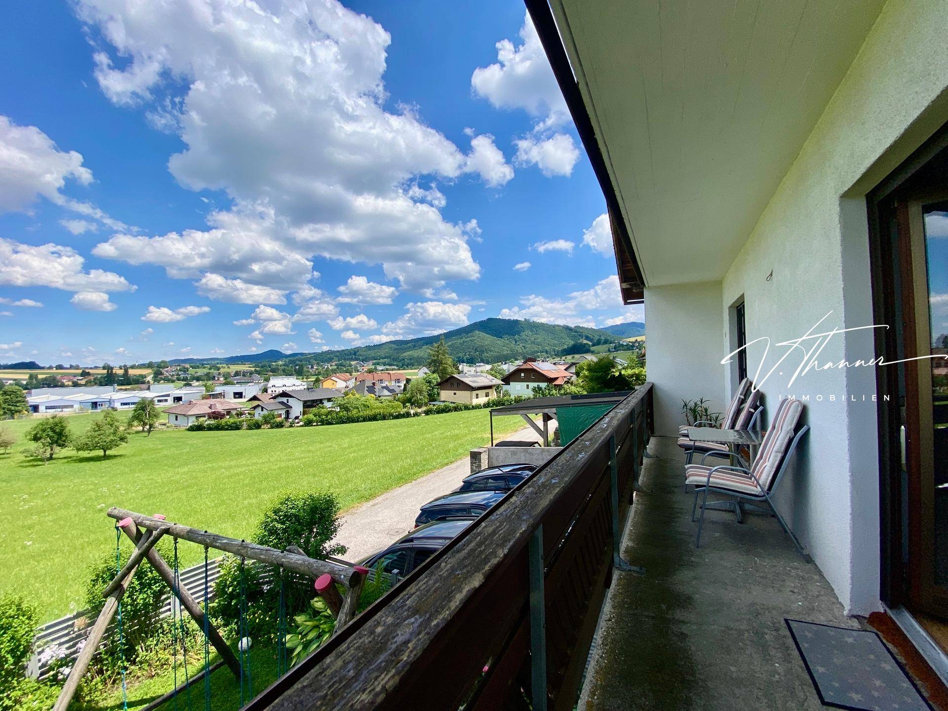 Langer Balkon mit Sitzgelegenheiten und Panoramablick über die grüne Landschaft und Berge.