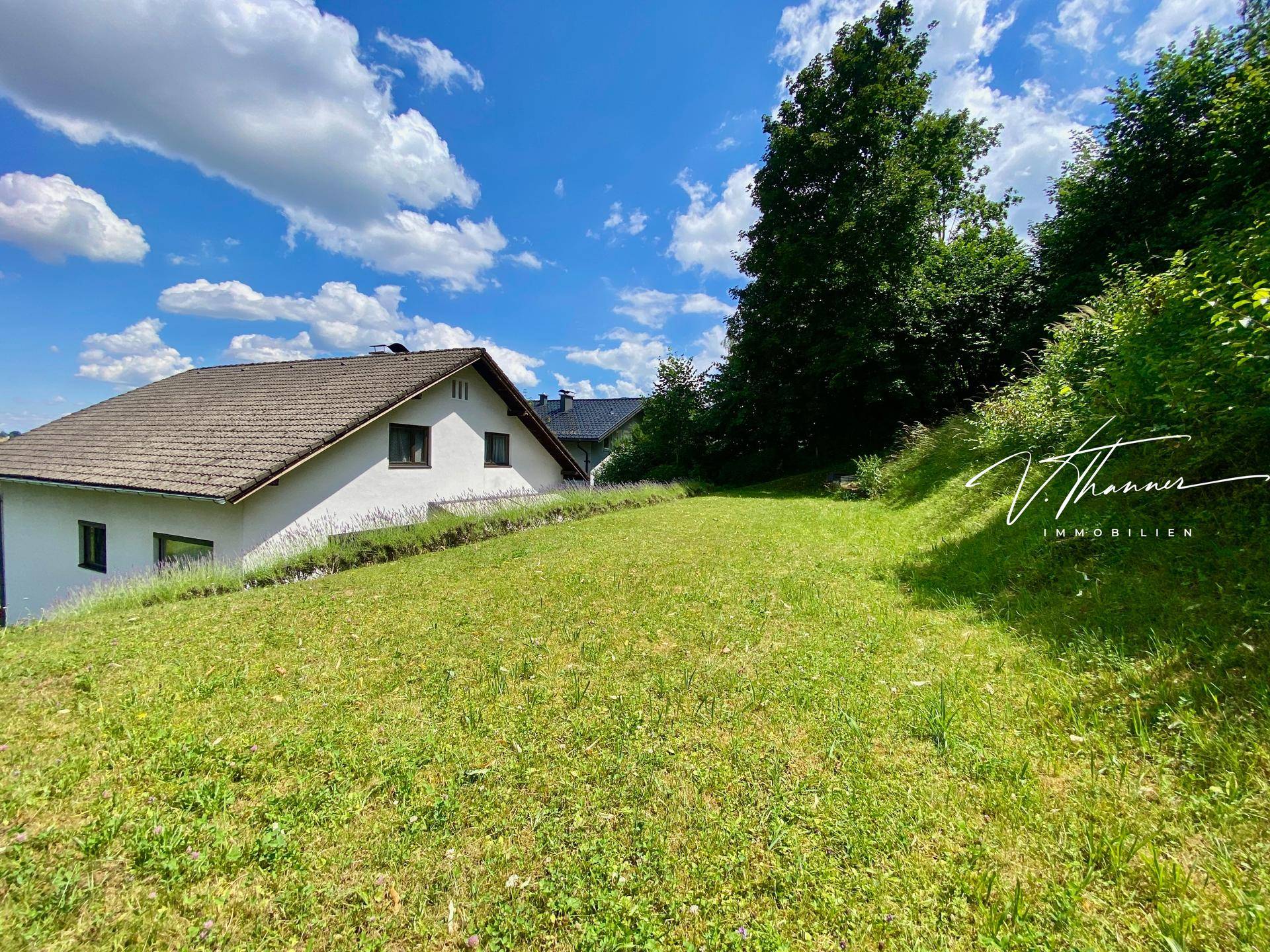 Weitläufige Rasenfläche des Gartens mit Blick auf das Haus und die umliegende Natur.