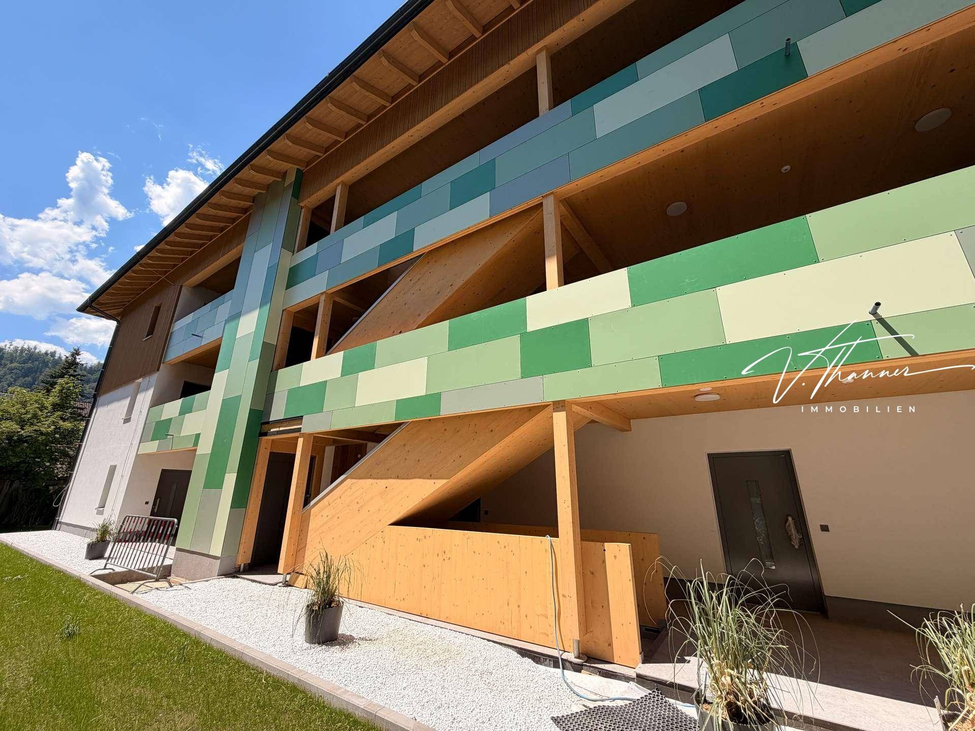 Moderne Gebäudefassade mit grünen Akzenten und Holzverkleidung, umgeben von Grünflächen.