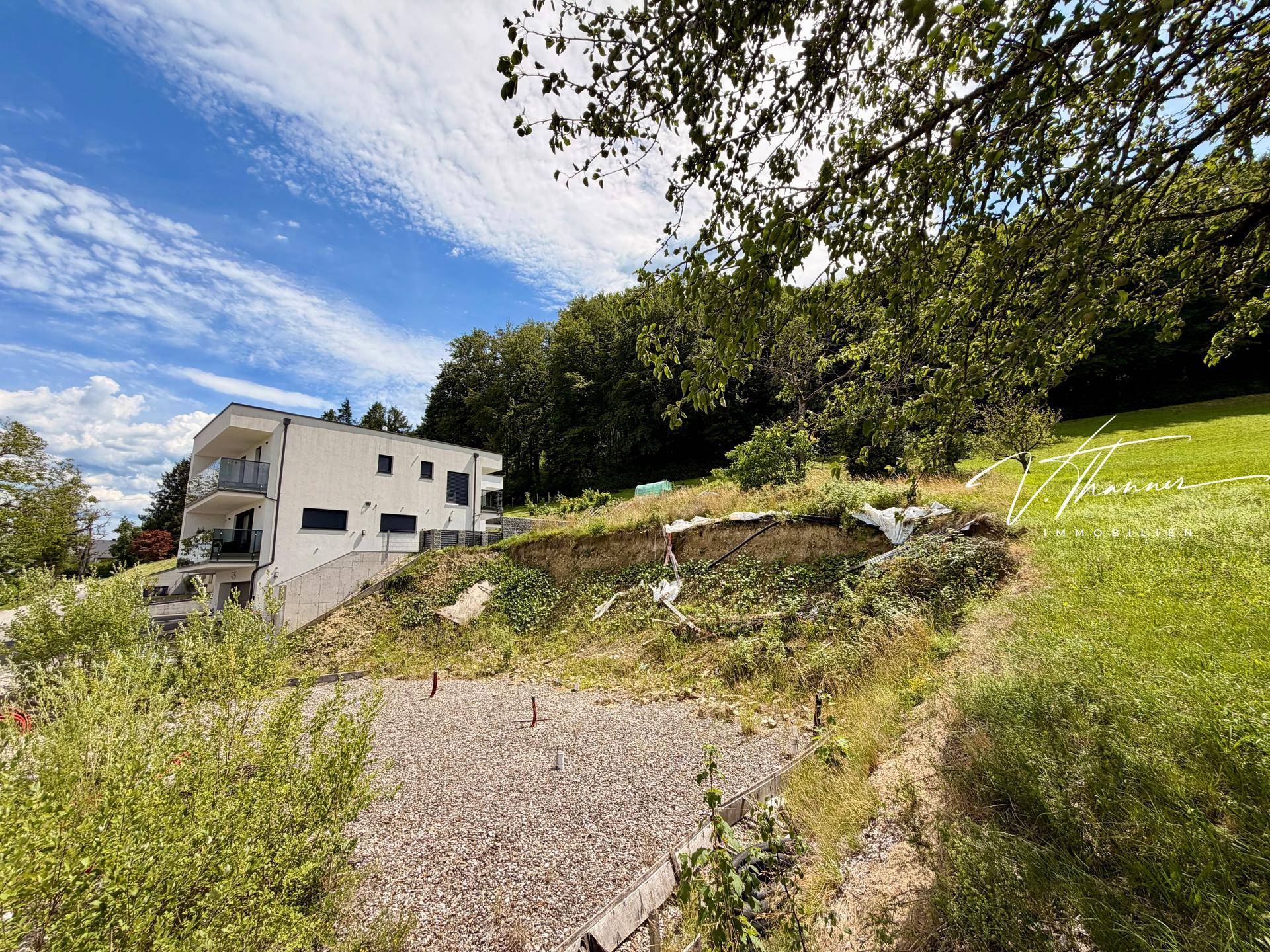 Modernes Wohngebäude mit Balkonen auf einem Hanggrundstück, umgeben von Natur und Wald.