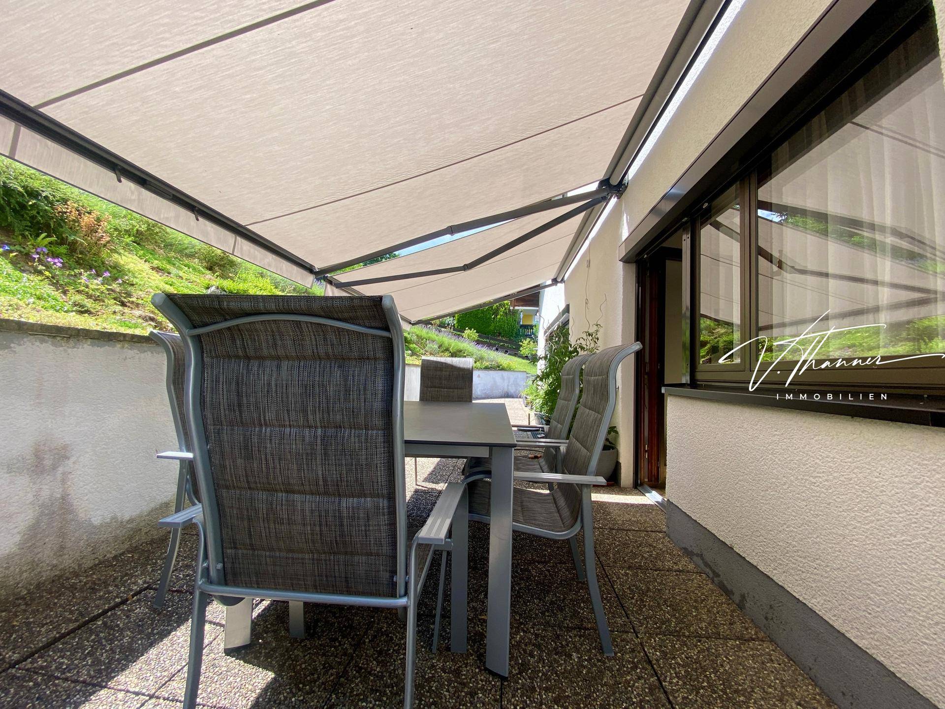 Gemütlicher Terrassenbereich mit Gartenmöbeln unter einer ausgefahrenen Markise.