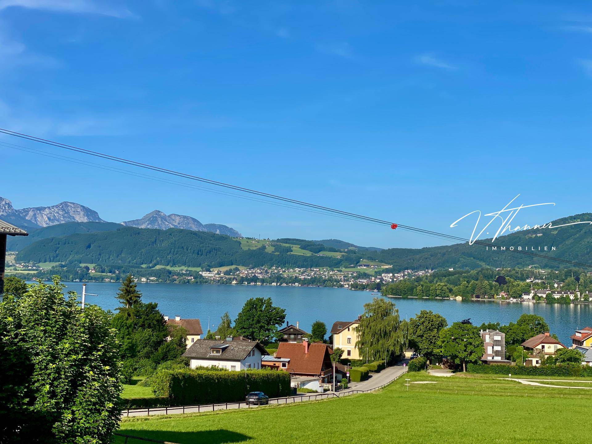 Weitläufiger Blick über einen idyllischen See mit charmanten Häusern am Ufer und einer beeindruckenden Bergkulisse.