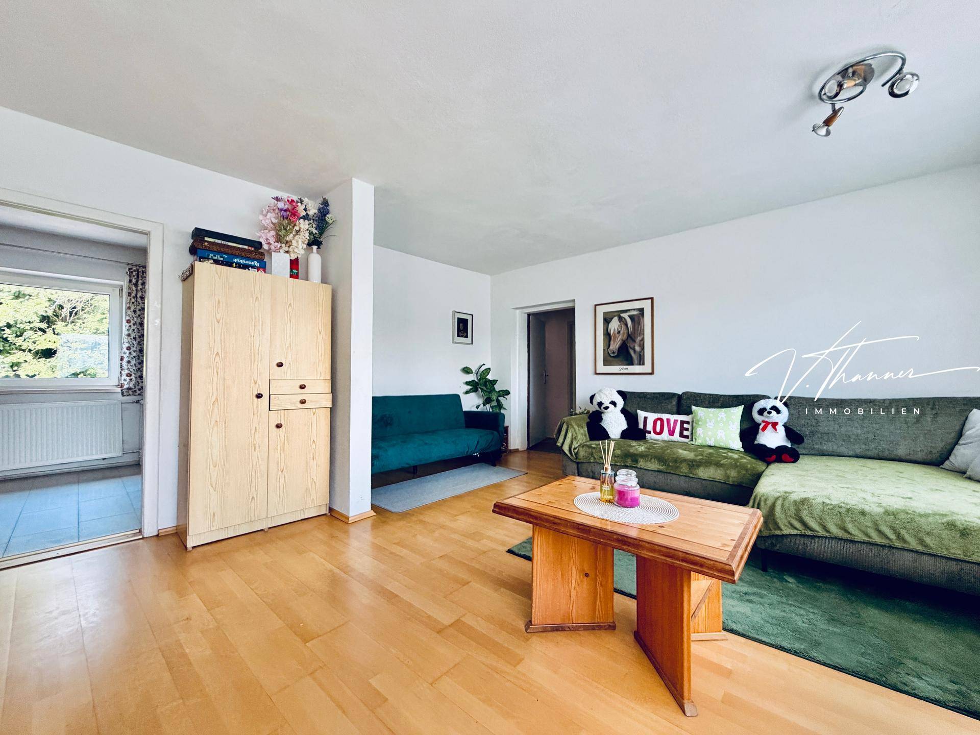 Gemütliches Wohnzimmer mit Holzboden, bequemen Sofas und einem Schrank aus hellem Holz.