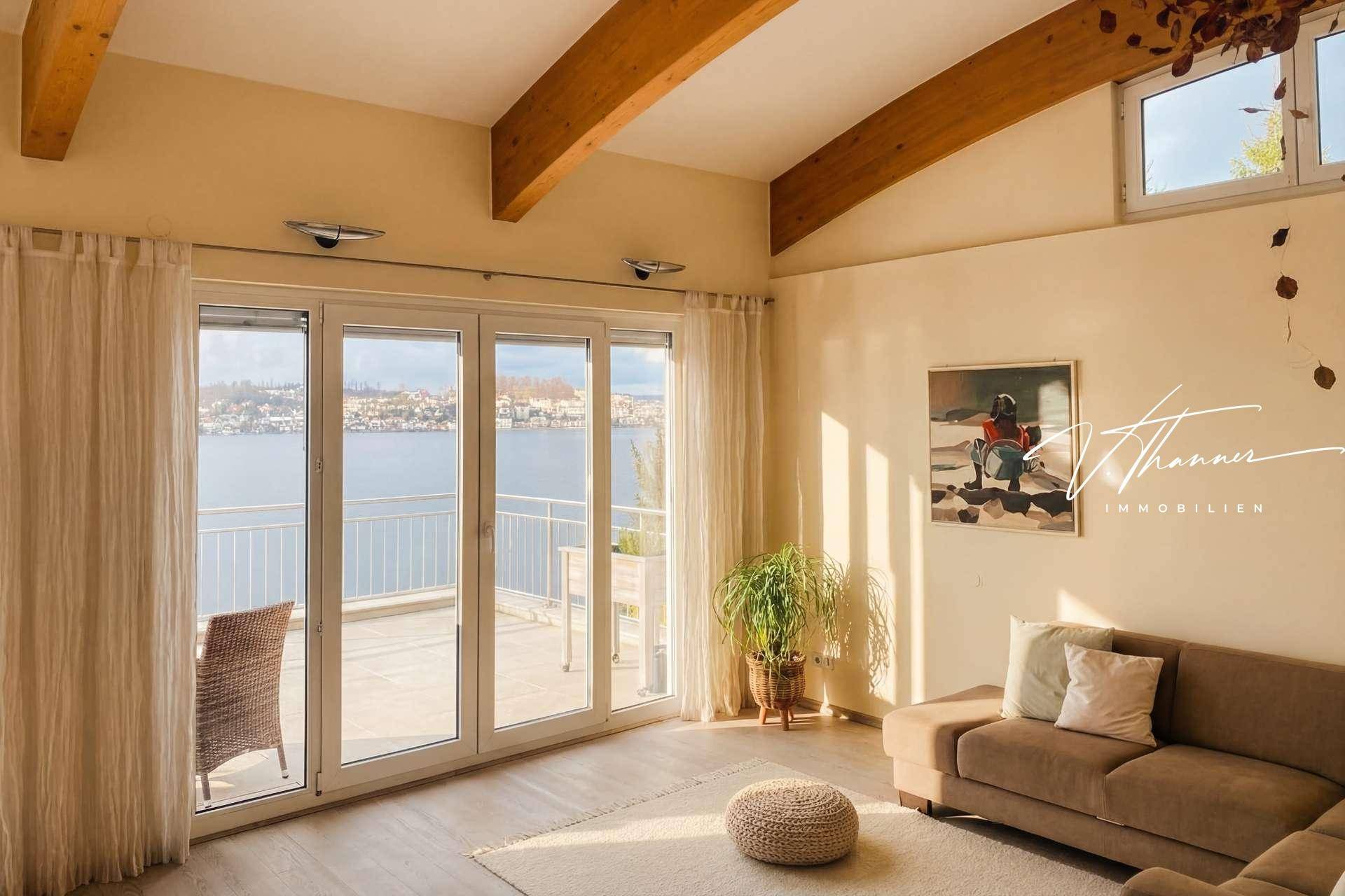 Gemütliches Wohnzimmer mit Sofa, Holzboden und Balkonzugang mit herrlichem Seeblick.