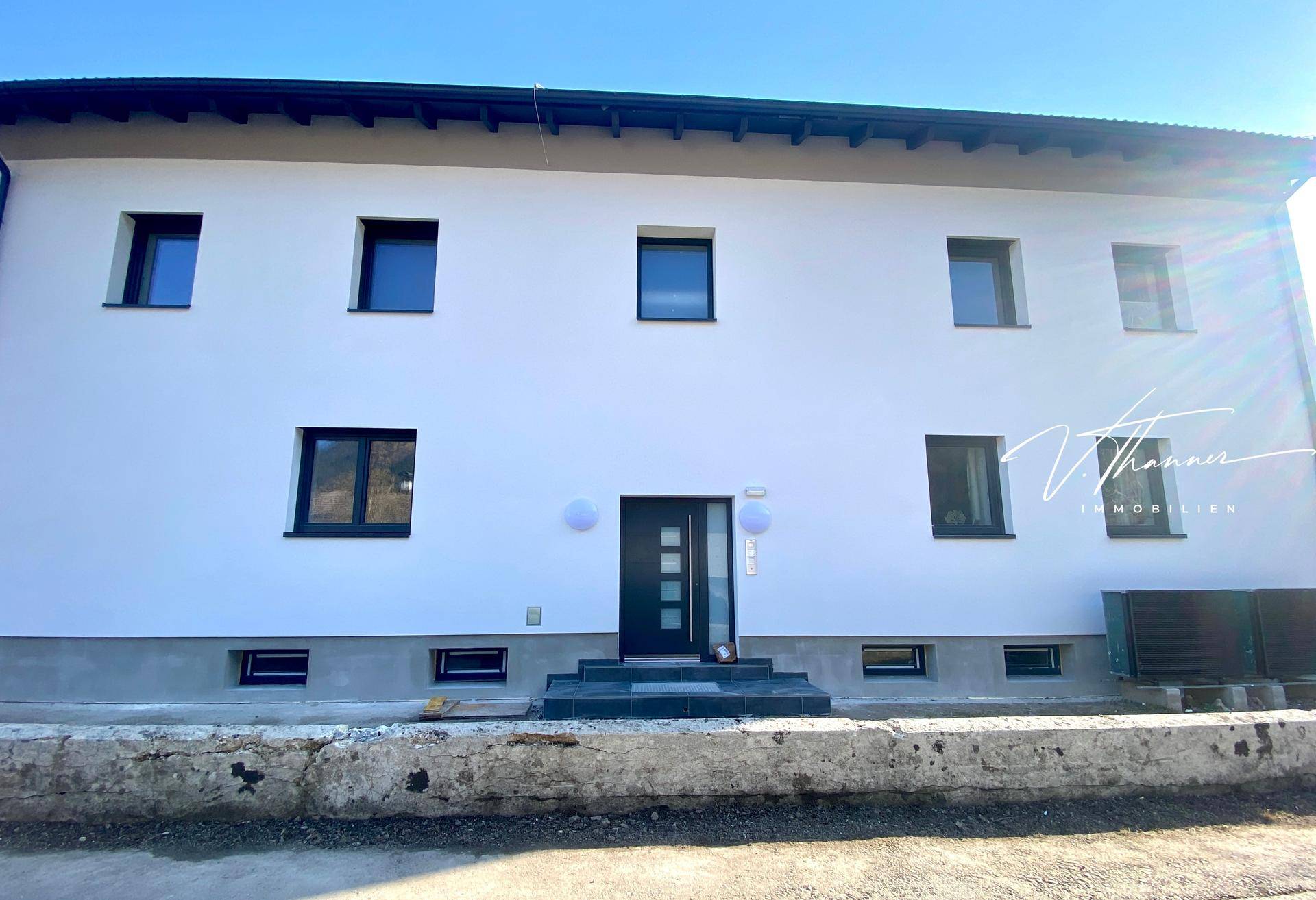Moderne Eingangsfassade des Neubaus mit dunkler Tür und mehreren Fenstern.