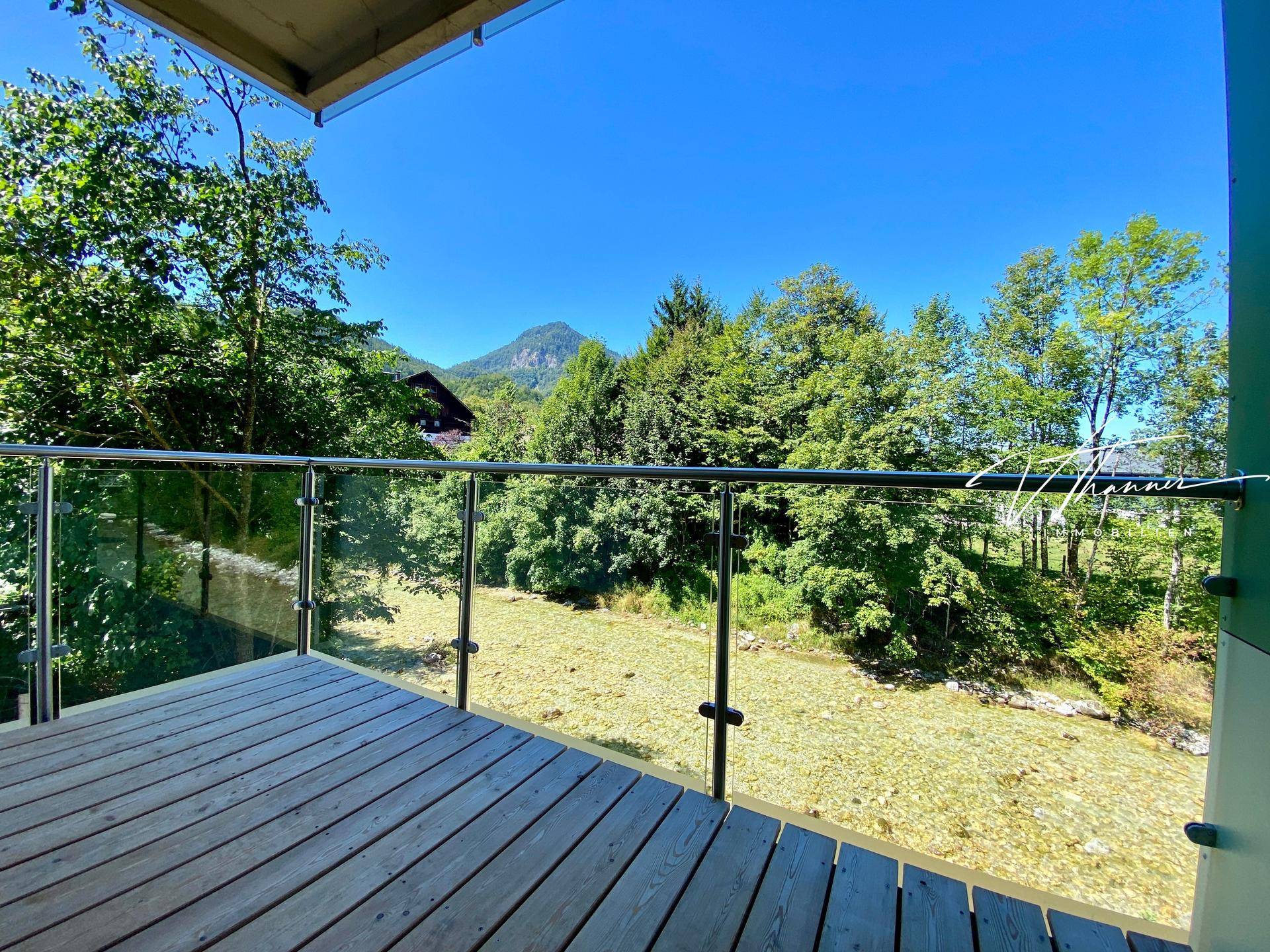 Geräumiger Balkon mit Glasgeländer und weitem Blick auf den Fluss und die umliegenden Berge.