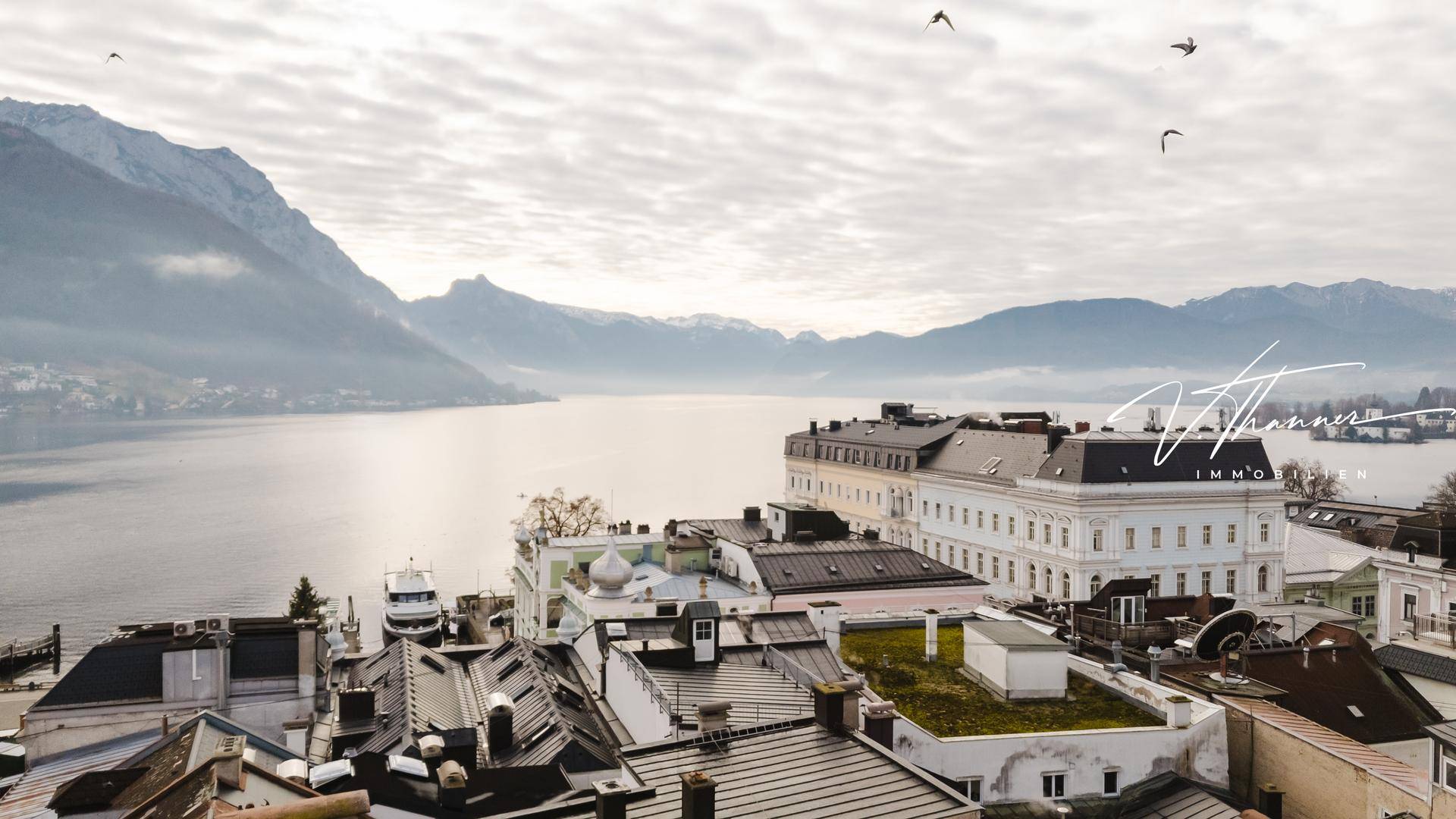 Malerischer Ausblick auf den See und die majestätischen Berge, umgeben von historischen Gebäuden.
