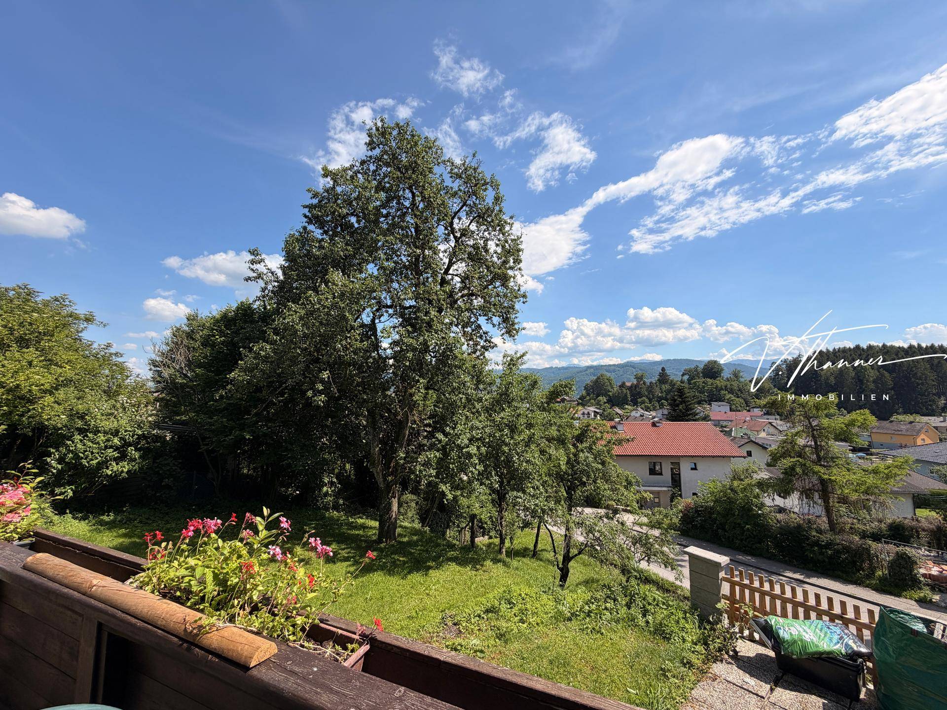 Panoramablick vom Balkon über die grüne Landschaft und die Dächer der umliegenden Häuser.