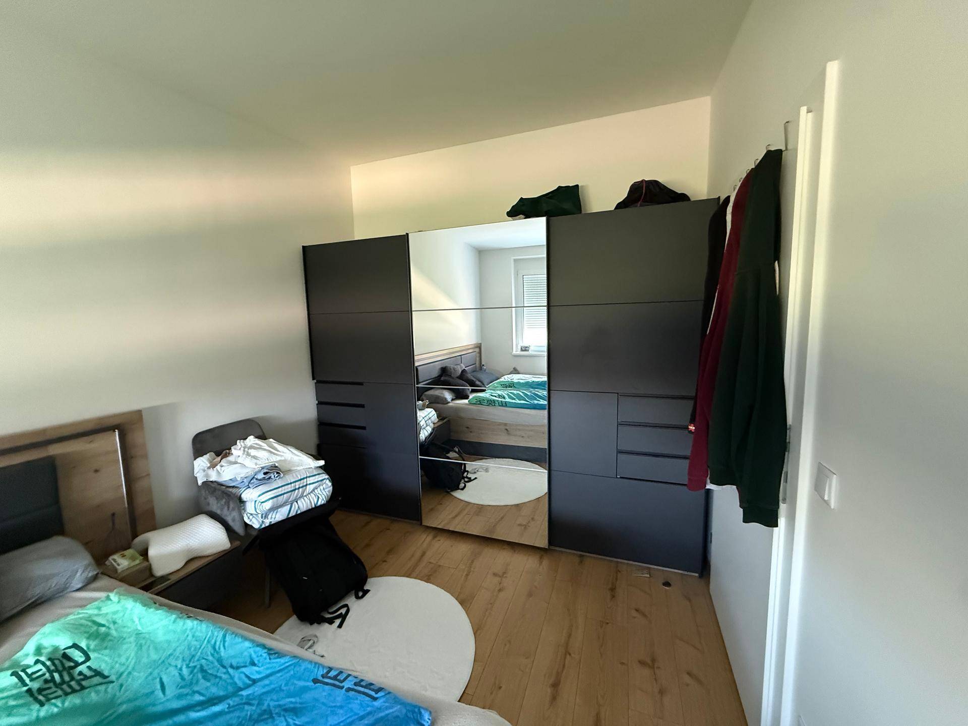 Schlafzimmer mit großem Spiegelschrank, Holzboden und Doppelbett.