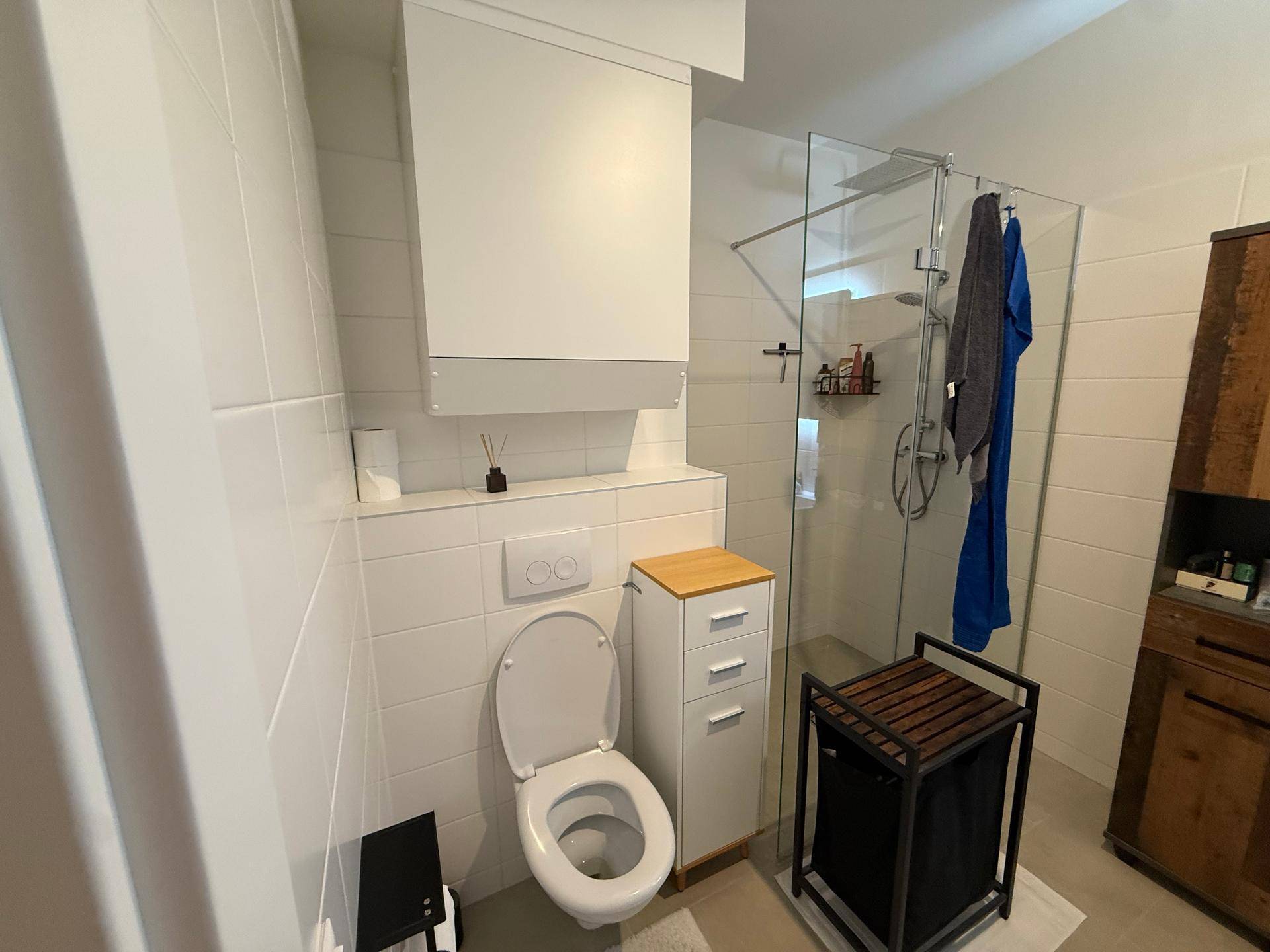 Helles Badezimmer mit Duschkabine, wandhängendem WC und weißen Fliesen.