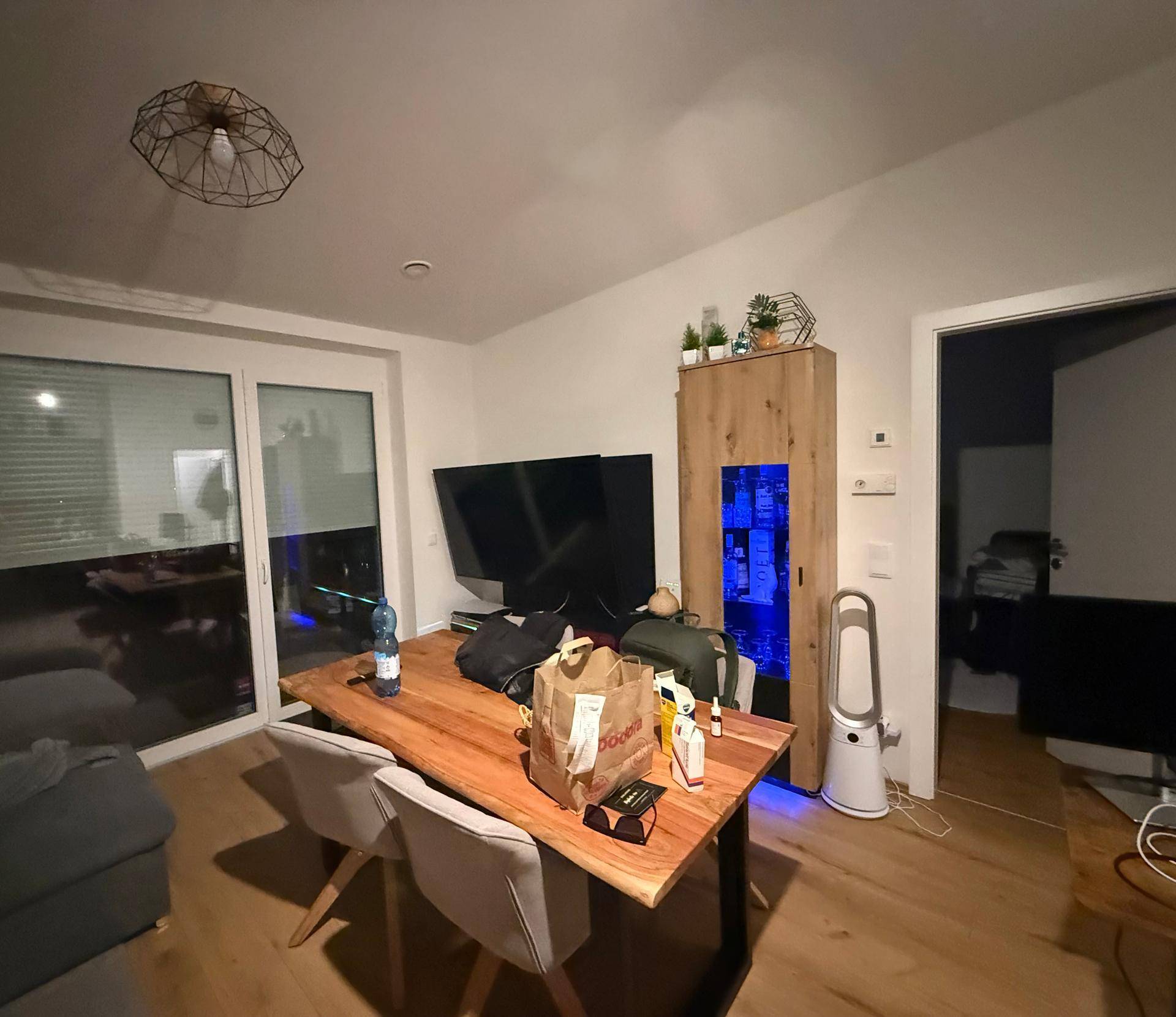Essbereich mit Holztisch, Stühlen und Zugang zu einem Außenbereich durch eine große Glastür.