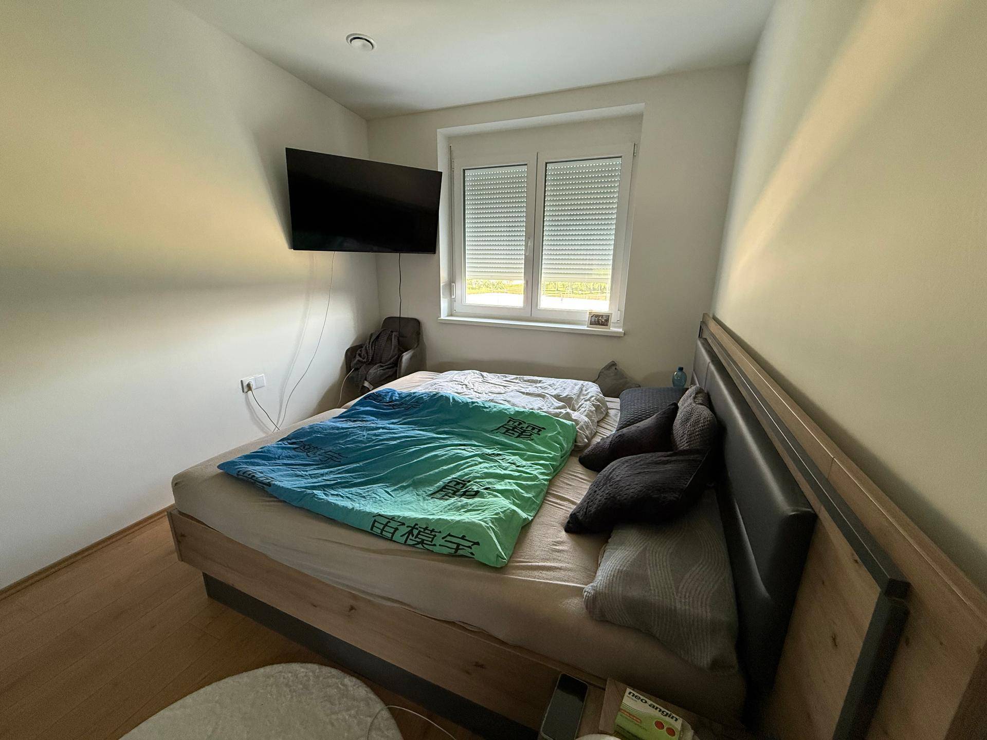 Schlafzimmer mit Doppelbett, Holzboden und Fenster mit geschlossenen Rollläden.