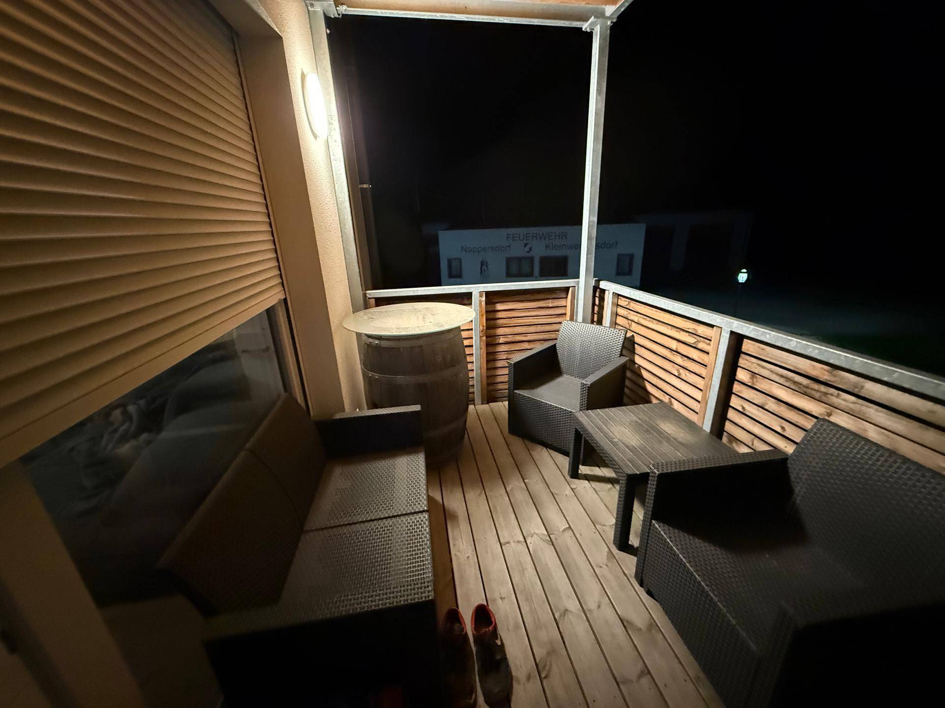 Gemütlicher Balkon am Abend mit Sitzgelegenheiten aus Rattan und Holzverkleidung.