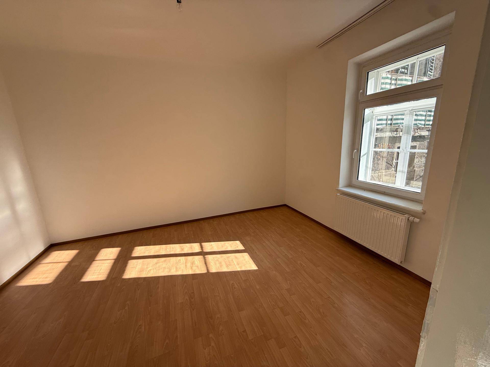 Lichtdurchfluteter Raum mit Laminatboden und Heizkörper unter dem Fenster.