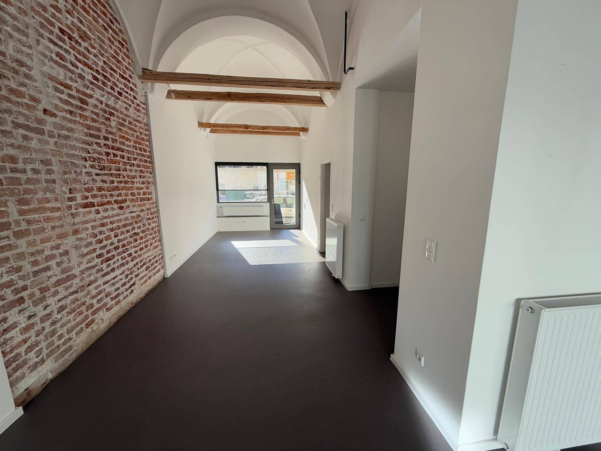 Langer Gewerberaum mit freigelegter Ziegelwand, Gewölbedecke und dunklem Bodenbelag.