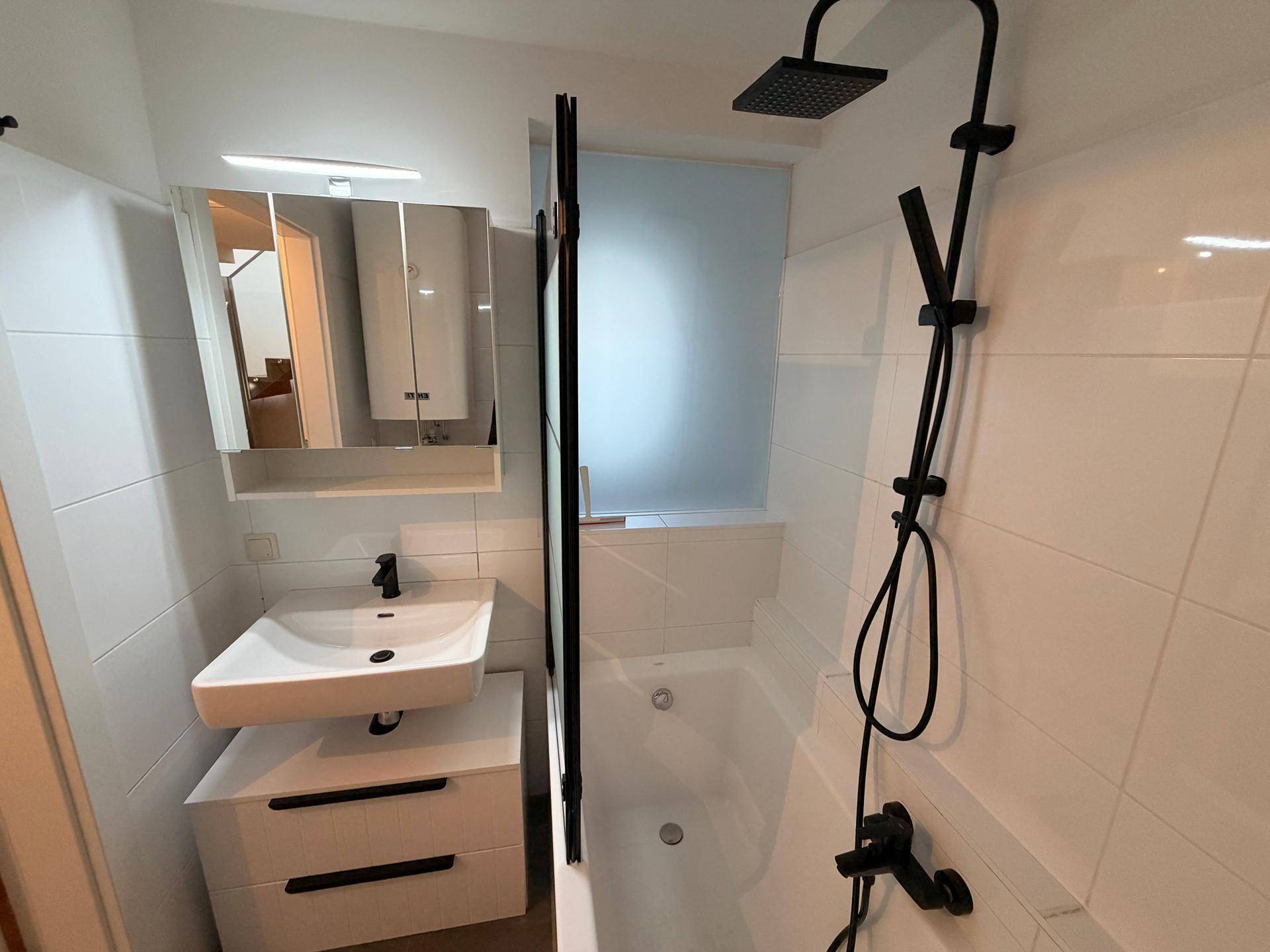 Modernes Badezimmer mit weißen Fliesen, Badewanne mit Duschwand und schwarzer Regendusche.